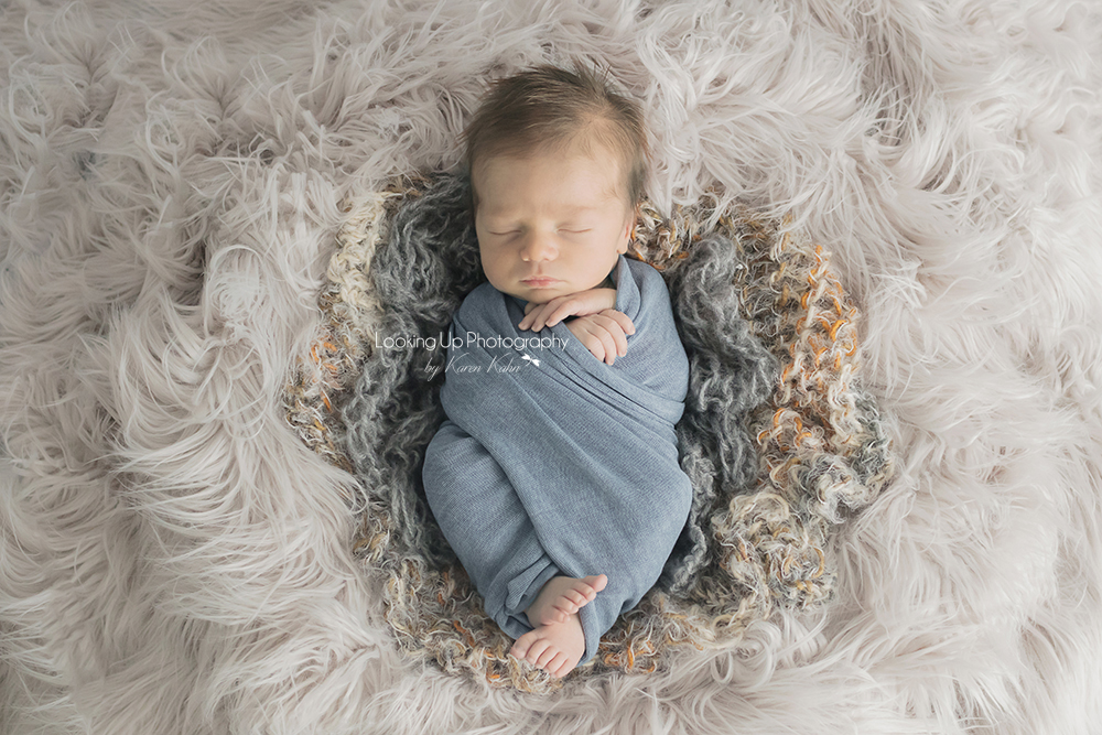 Cozy baby boy swaddled in neural tones of blue with gray fur for newborn session baby portrait