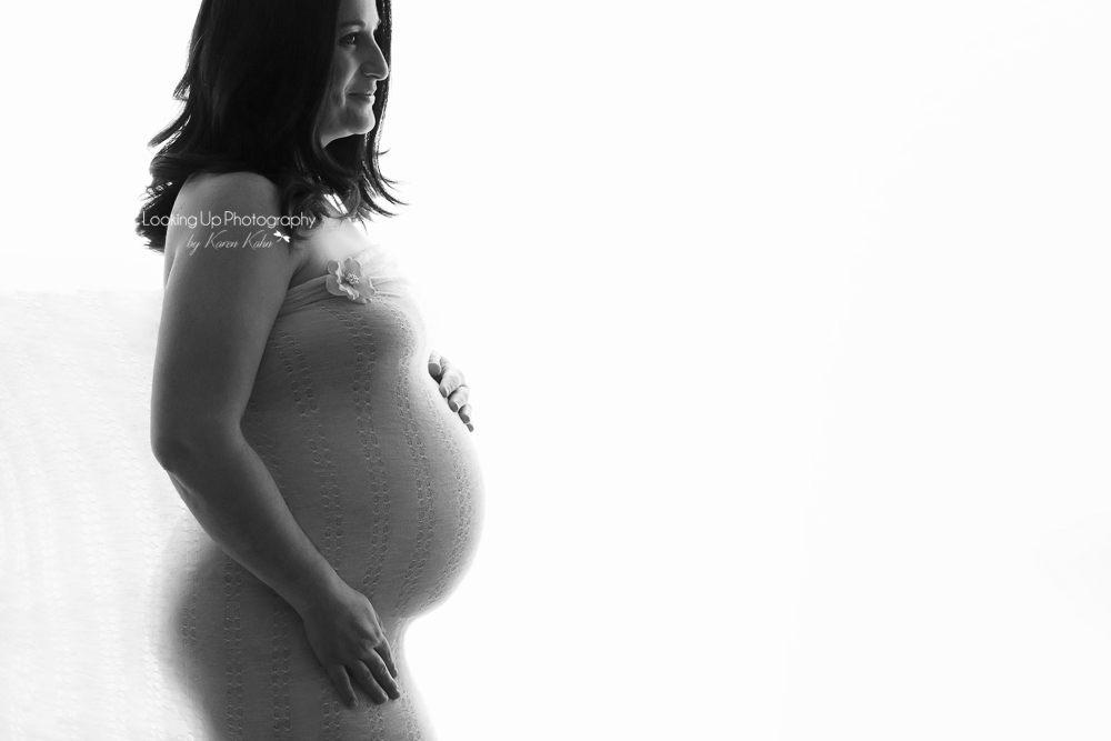 Black and white back-lit expecting mommy draped in lovely lace fabric cradling belly for posed maternity portrait session