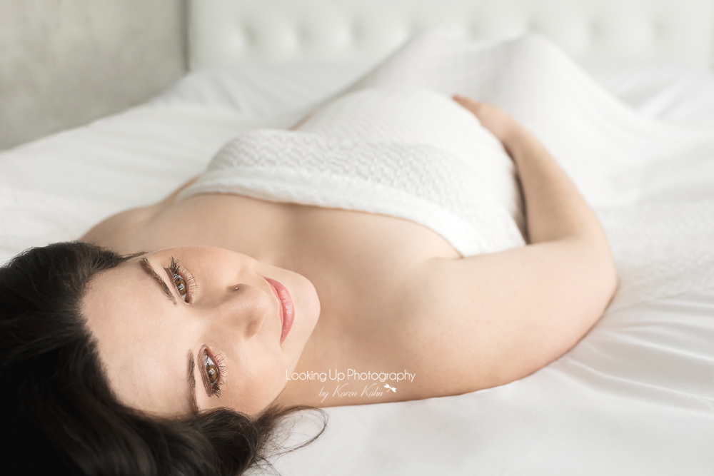 Expectant Mommy posed on bed with delicate white fabric for glamor maternity portrait session