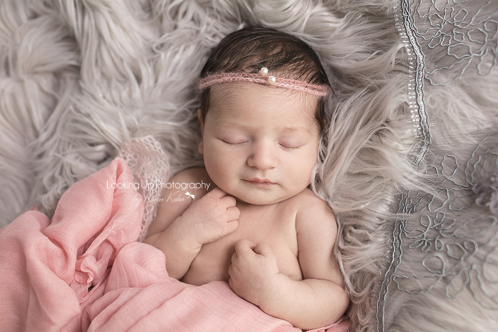 Newborn portrait with smiling baby dressed in soft pink fabric and pearl headband with gray lace and cozy fur and tiny hands posed for baby girl session