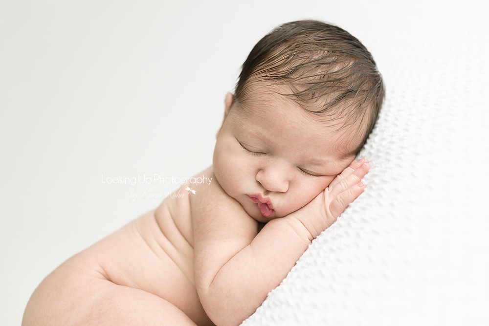 Sleepy baby girl with lovely hair and pouty lips posed on white blanket for newborn portrait session