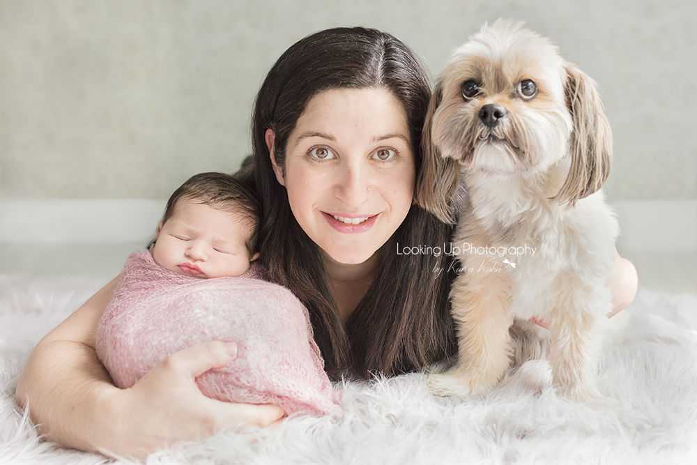 Adorable pet dog with mommy and newborn cuddling with sweet pink lace wrap for baby girl portrait session