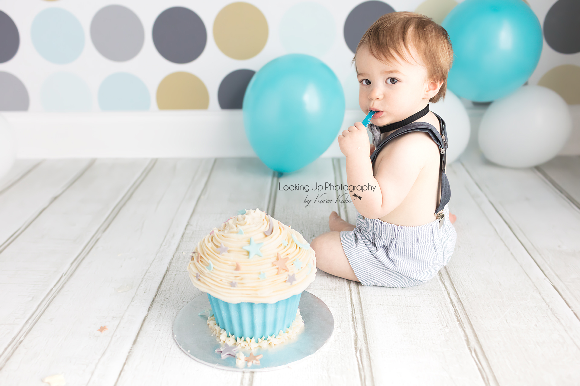 12 month old baby boy donning bow tie and suspenders eating cake in stylish blues and grays and polka dots for cake smash session 1 year milestone portrait