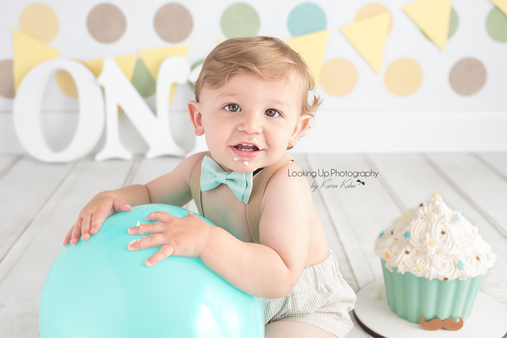 12 month celebration for baby boy looking snazzy in bow tie and suspenders with polka dots and mustache cake for One year old milestone portrait cake smash session