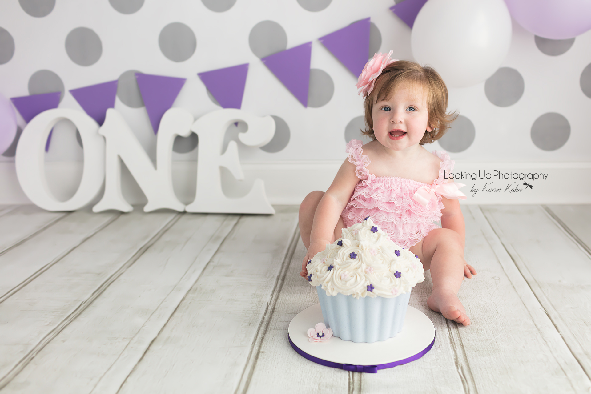 Pretty in pink 12 month milestone for baby girl looking sweet in lace and flower hair bow with gray polka dots for cake smash session one year old portrait