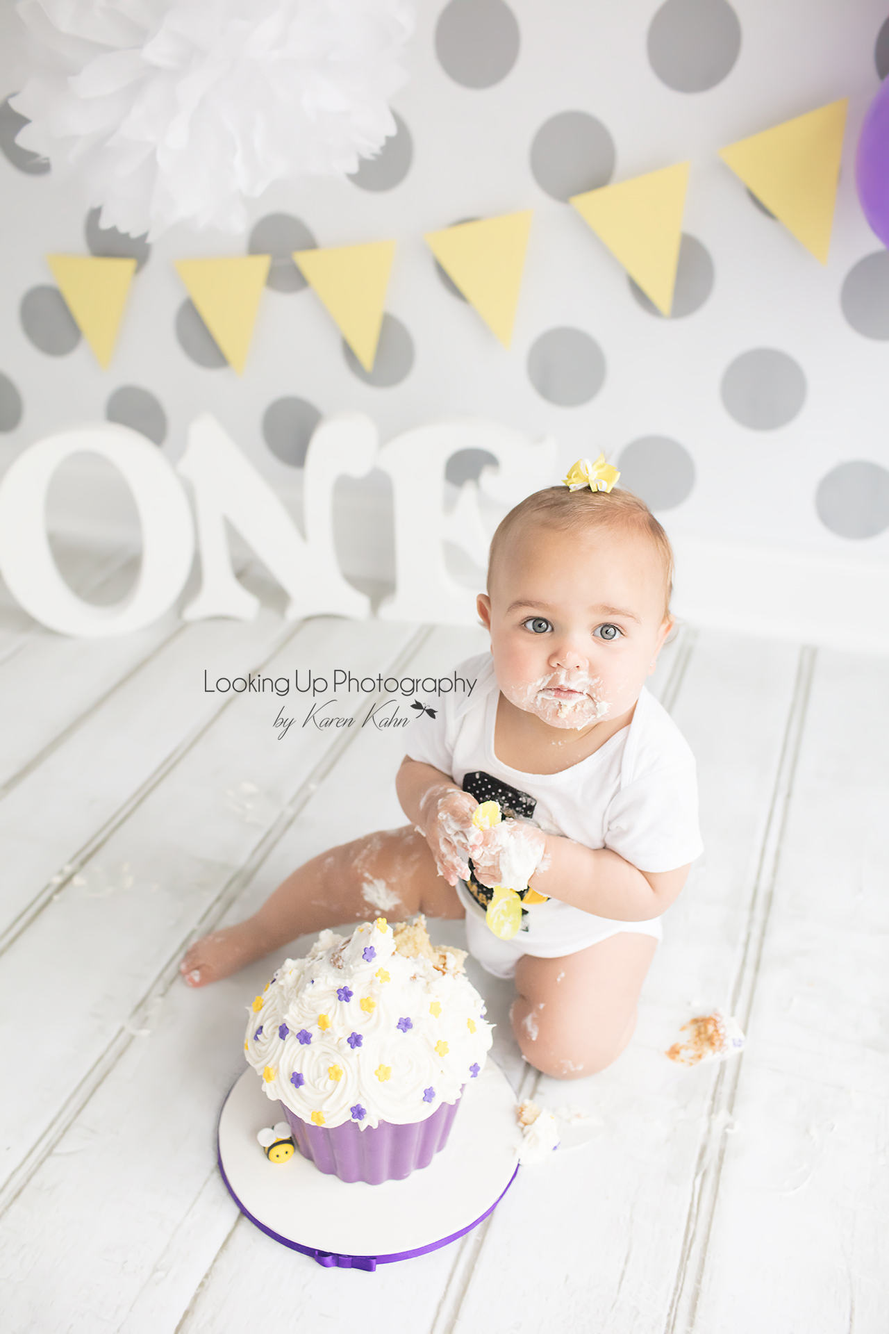Cake smash session with bumble bee theme for one year old milestone baby girl looking adorable in yellow and white with gray polka dots for 12 month portrait