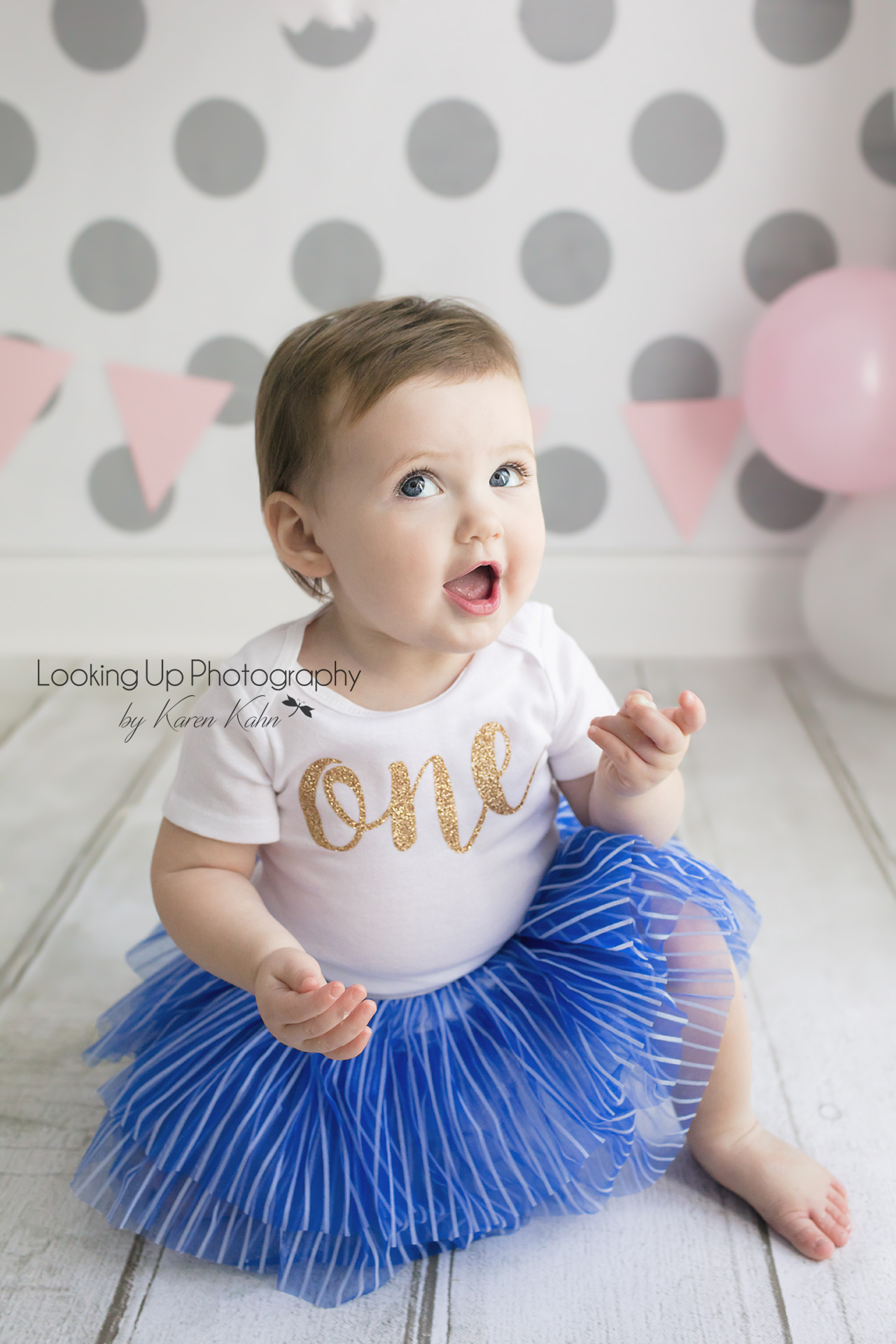 Laughing cutie pie in gold and blue tutu cake smash session for 12 month portrait baby girl looking sweet with gray polka dots for one year old milestone