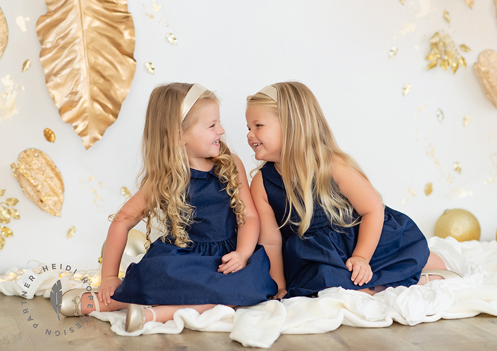 Twin sisters giggling dressed in pretty blue dresses for fun Joyful Gatherings gold set design in Fall holiday family portrait session