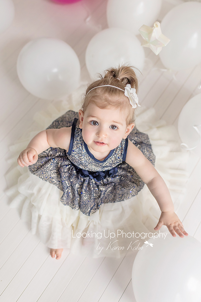Baby girl in blue lace dress and white balloons for 12 month milestone 1st birthday portrait session