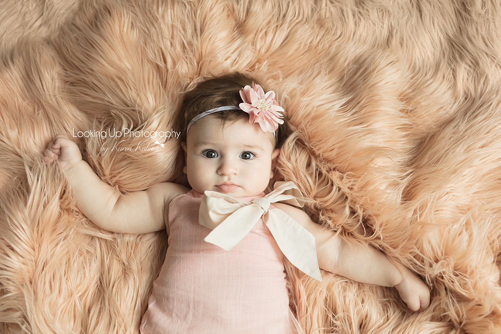 Portrait session aerial view of baby girl laying on peach fuzzy blanket and pink flower headband for 4 month milestone