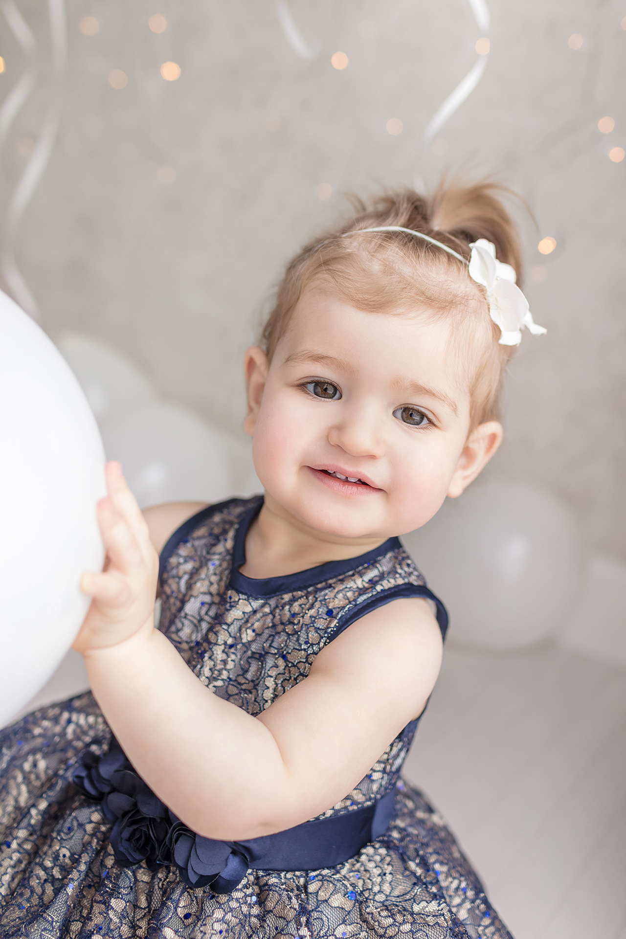 1st birthday milestone portrait session with happy 12 month old baby girl in blue lace dress and white balloons and sparkle 