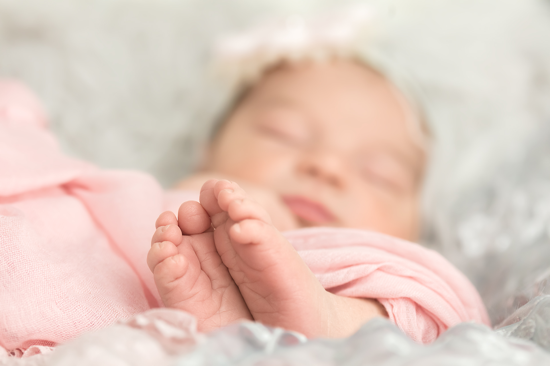 Newborn portrait session of Baby girl swaddled in a pink wrap with focus on tiny toes
