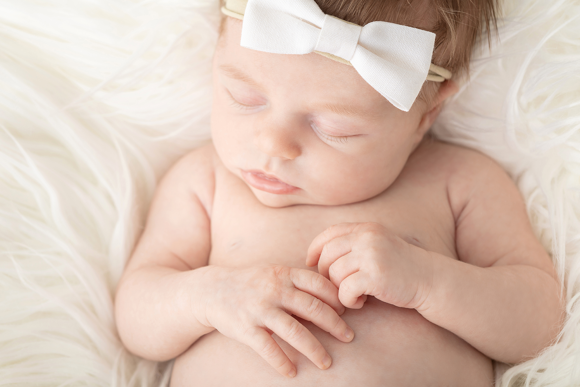 newborn baby girl with strawberry blonde hair sweetly sleeping on an ivory flokati, wearing an ivory bow on a stretch headband for newborns