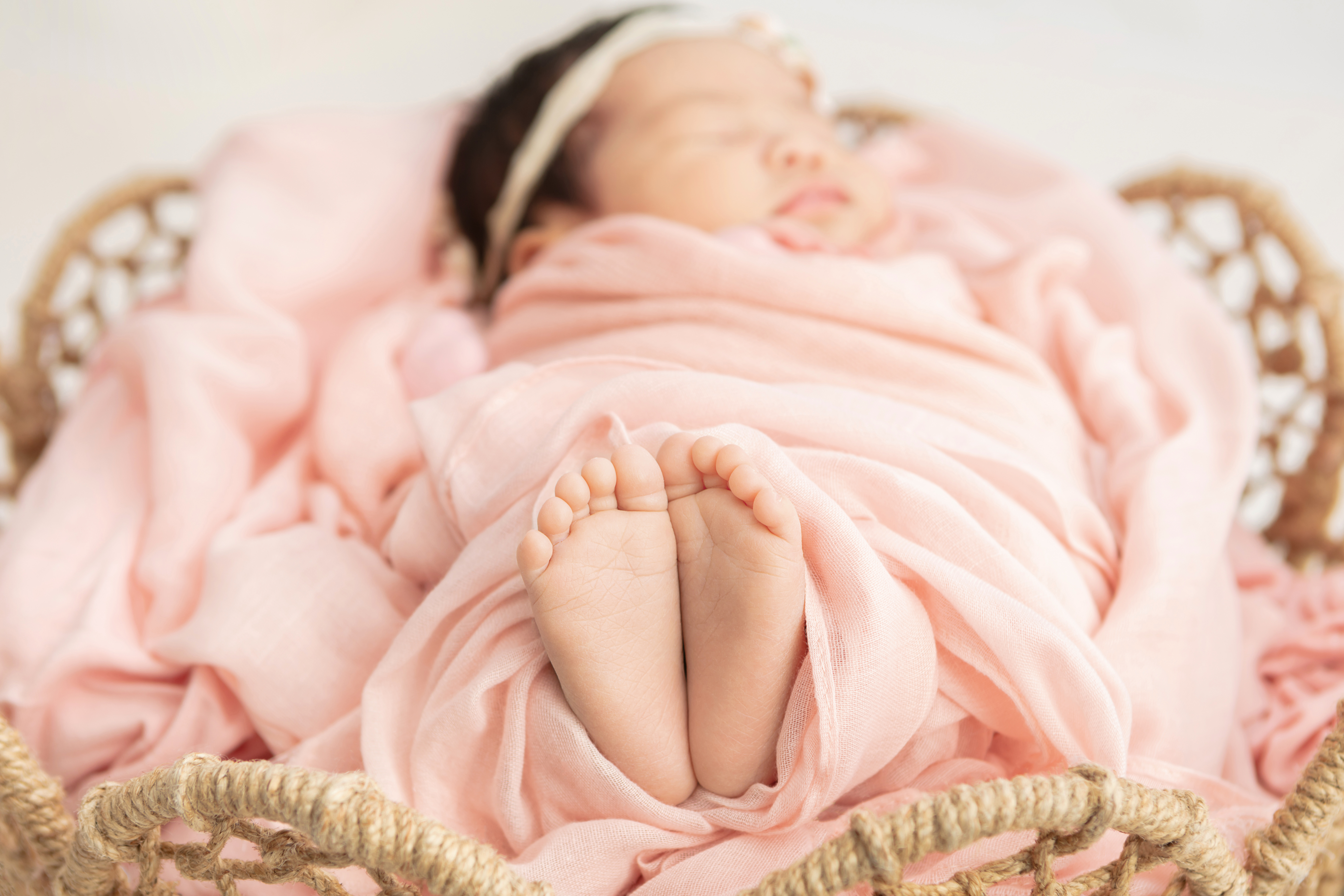 closeup of baby feet and toes with baby's napping face in the background, peachy pink swaddle