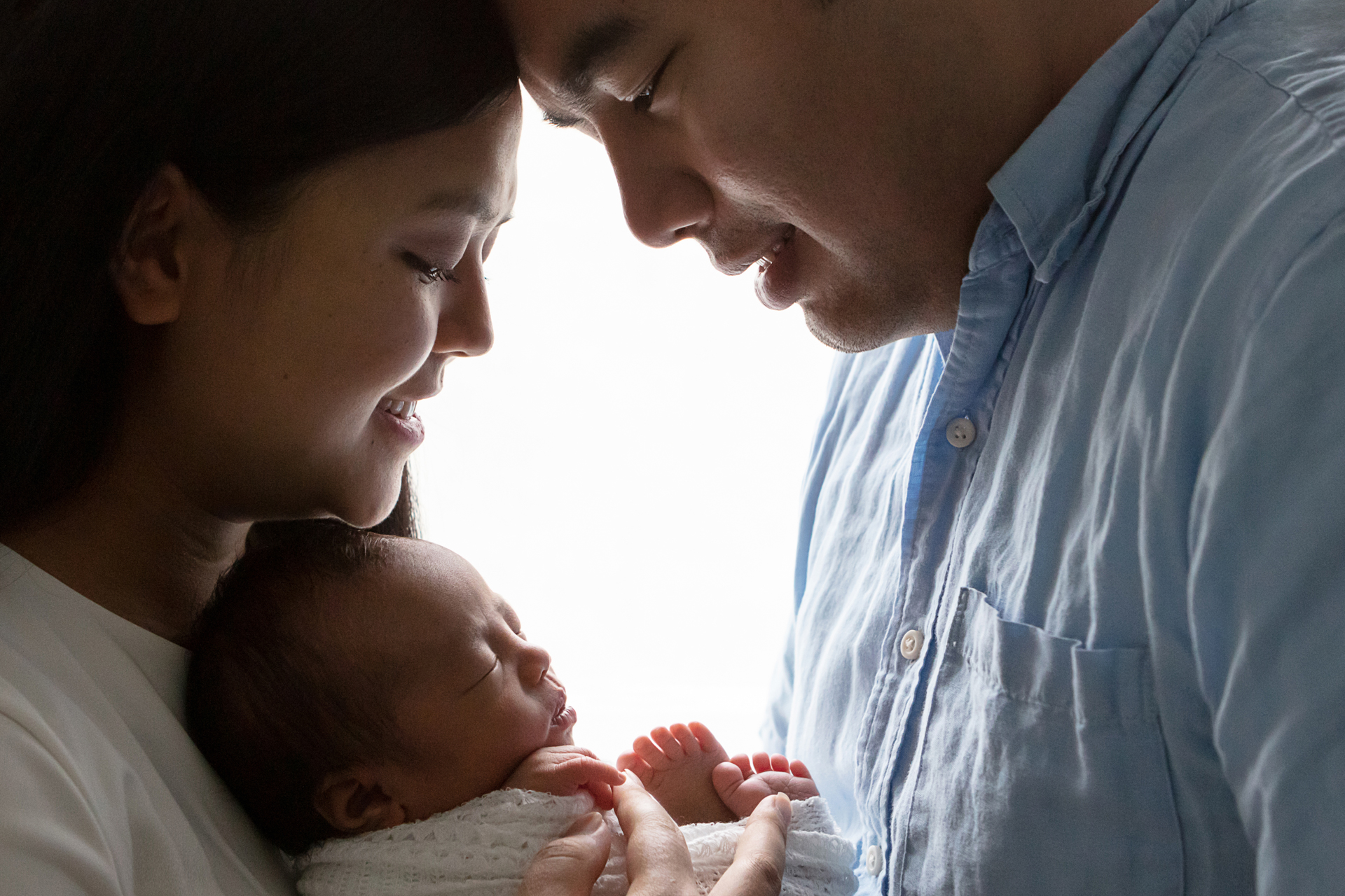 backlit image of a mother and father silhouetted and looking down at their newborn daughter