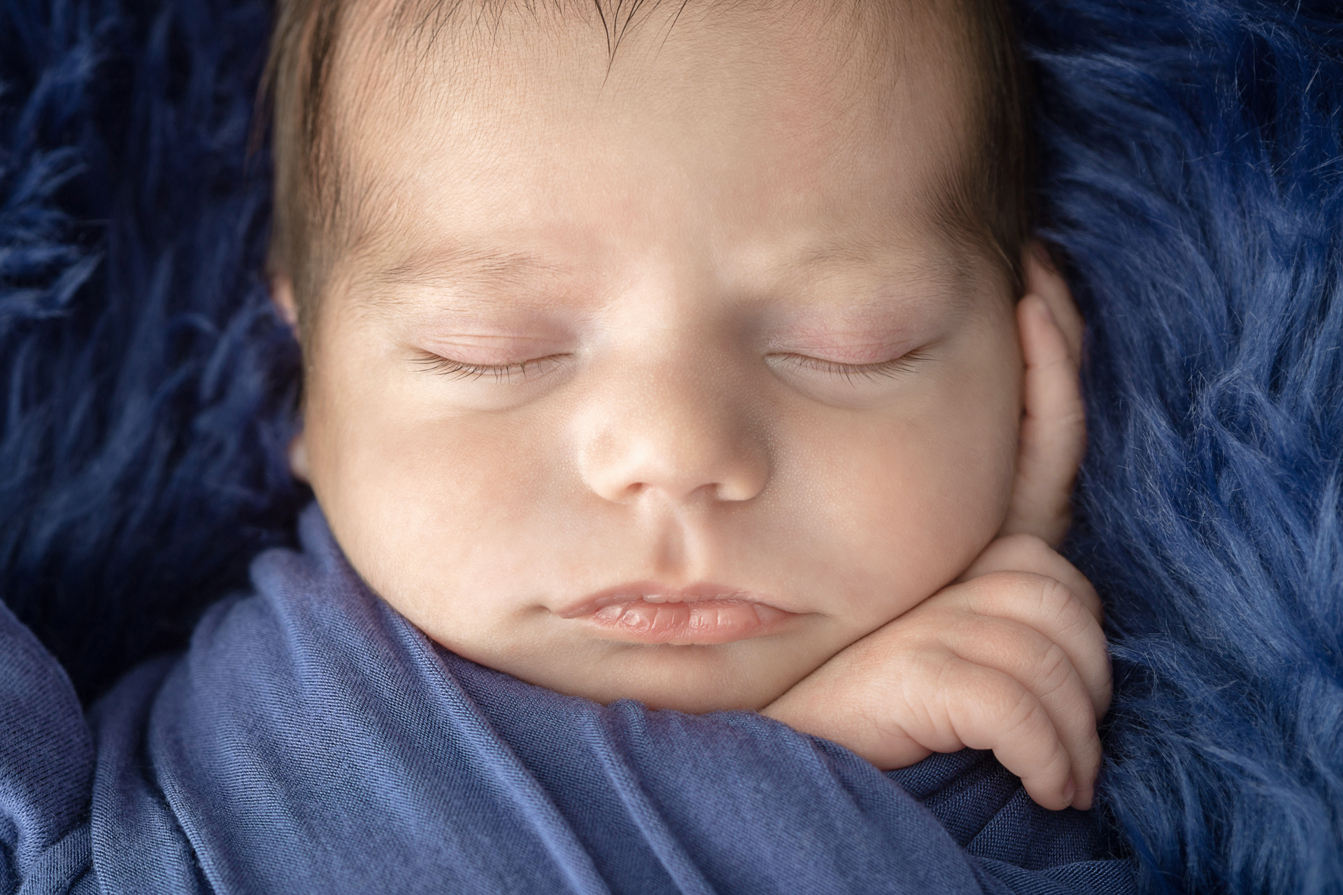 closeup image of the details of a newborn baby's face with his hands holding the swaddle and gently resting next to his head