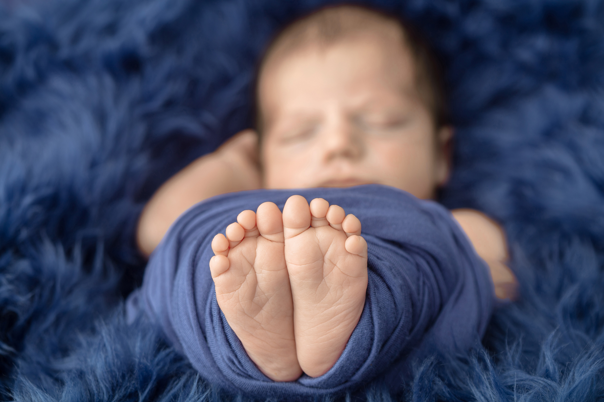 closeup photograph of the feet and toes of a new baby peeking out of a navy swaddle; navy flokati