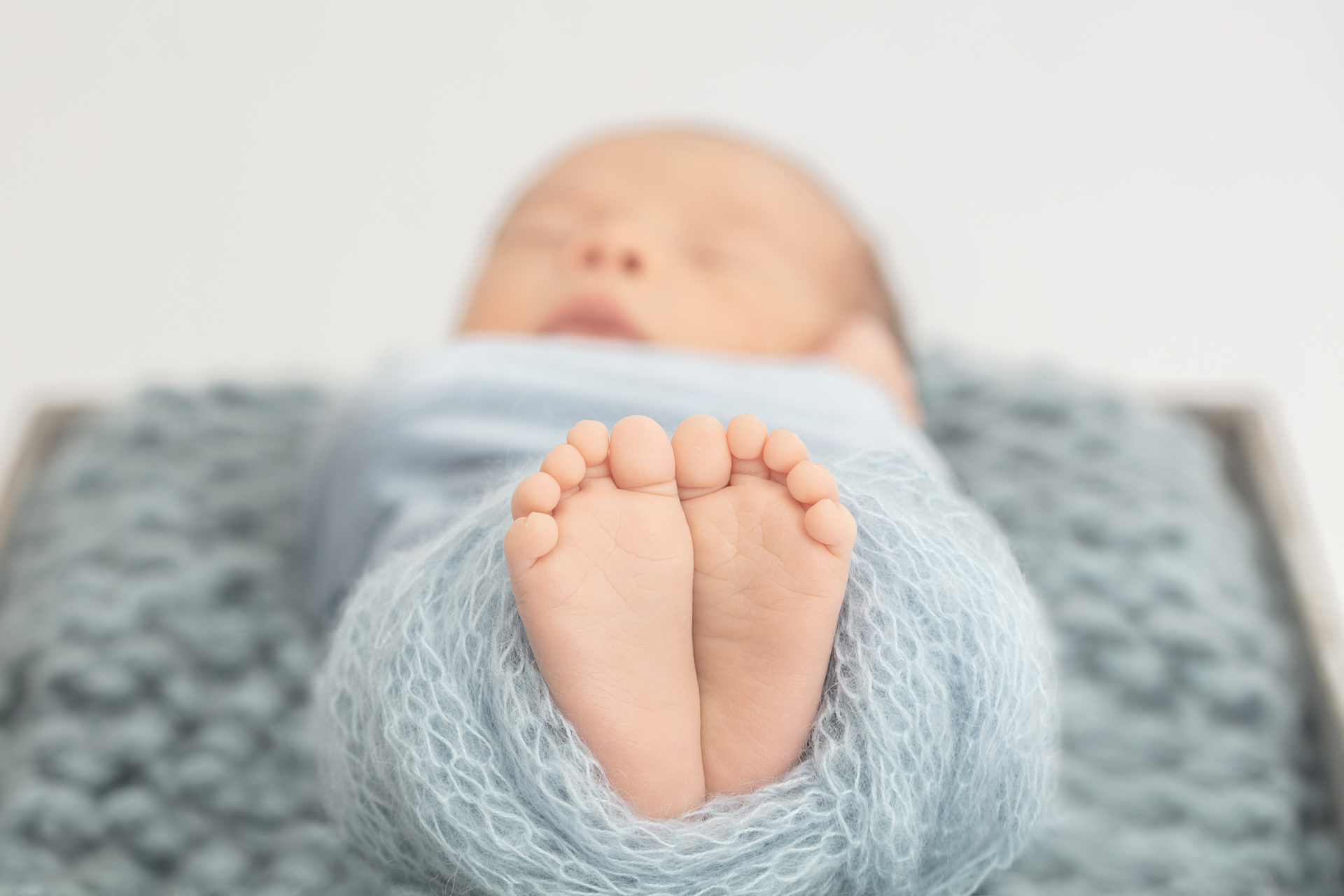 details of a baby boy's feet peeking from an open knit light dusty blue blanket; Looking Up Photography