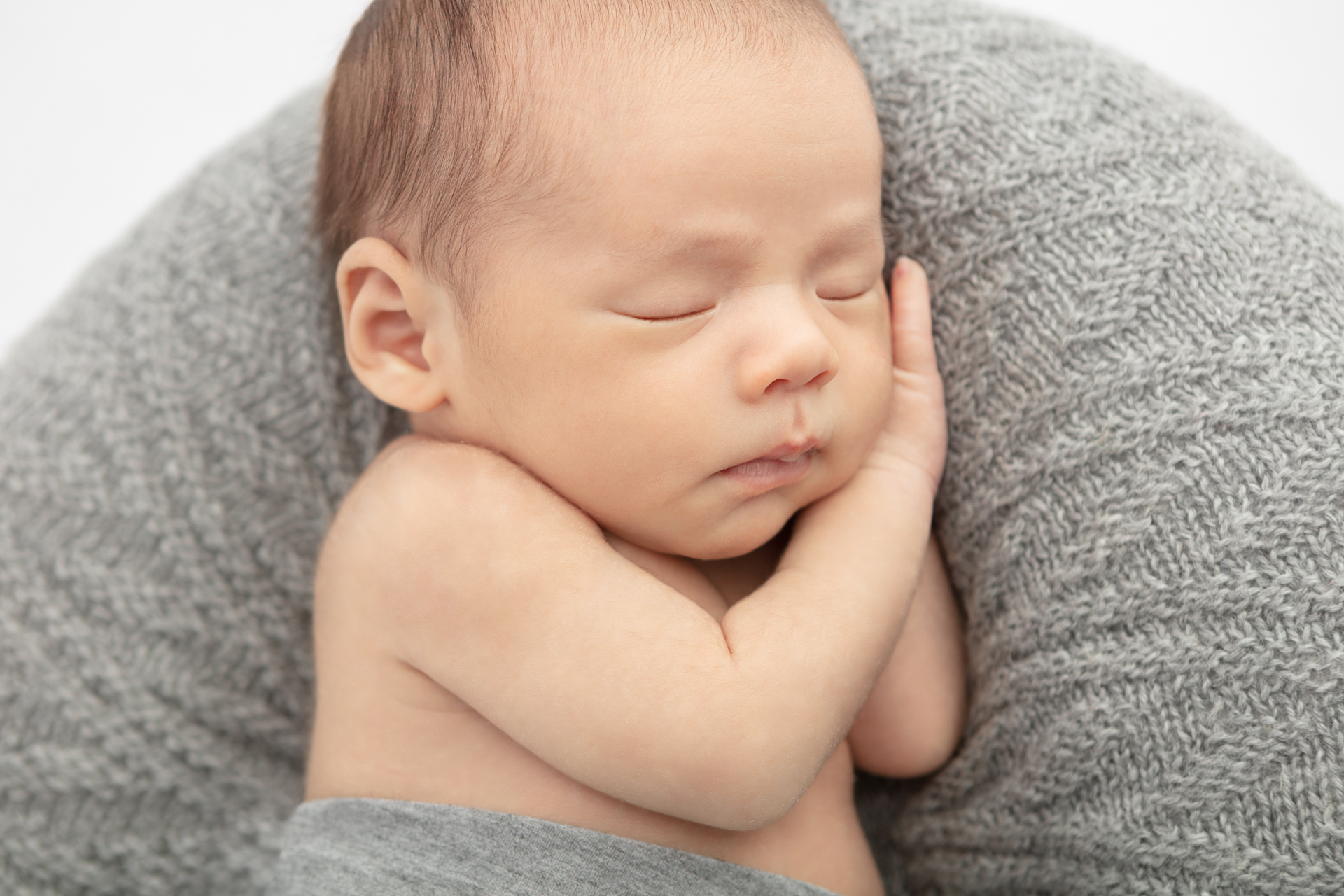 sleeping newborn baby boy wrapped in a gray swaddle with his hands folded under his head