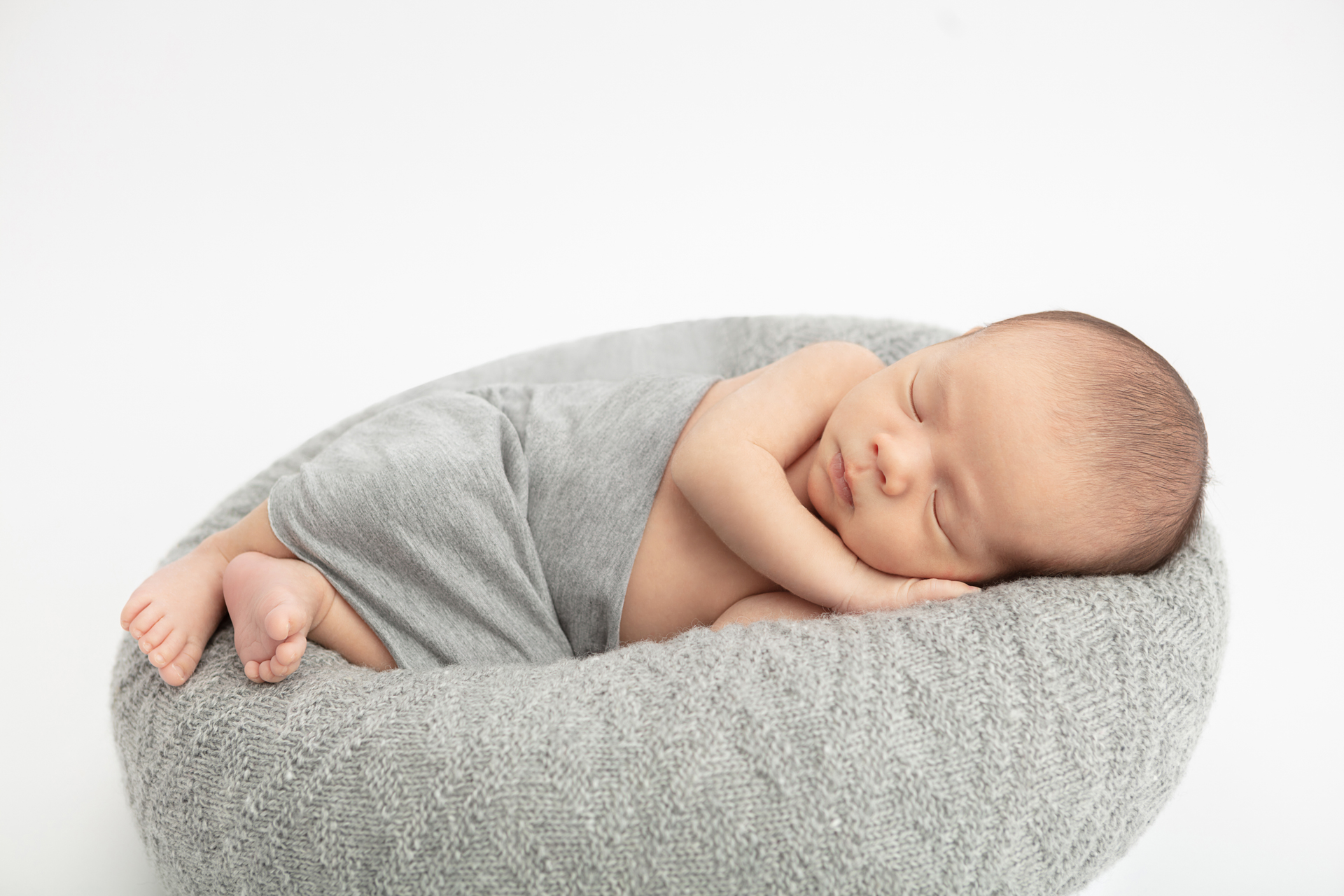 newborn baby boy wrapped in a gray heather swaddle and lying on a gray knit pouf