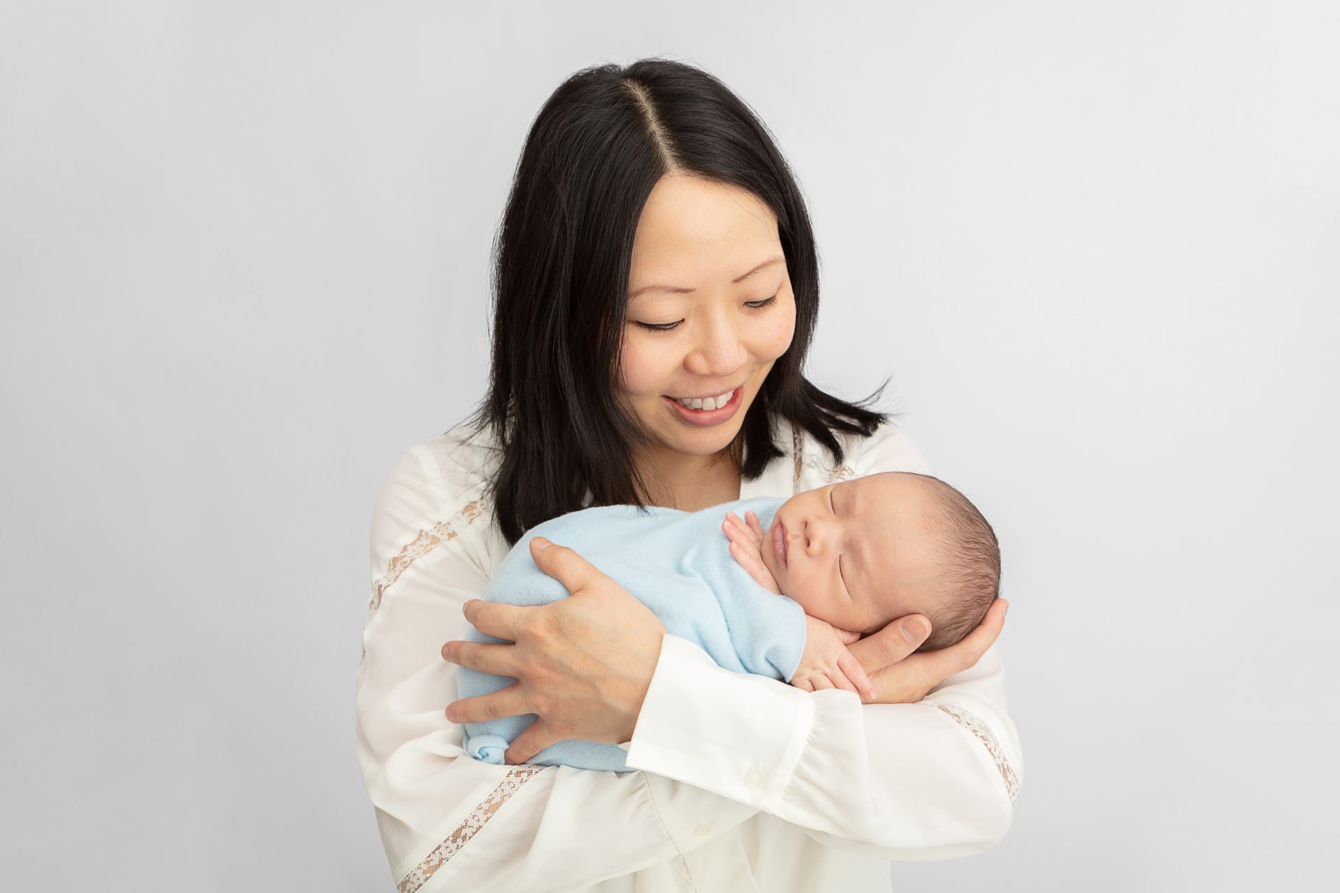 happy new mom holding her newborn baby in her arms, who is swaddled in blue