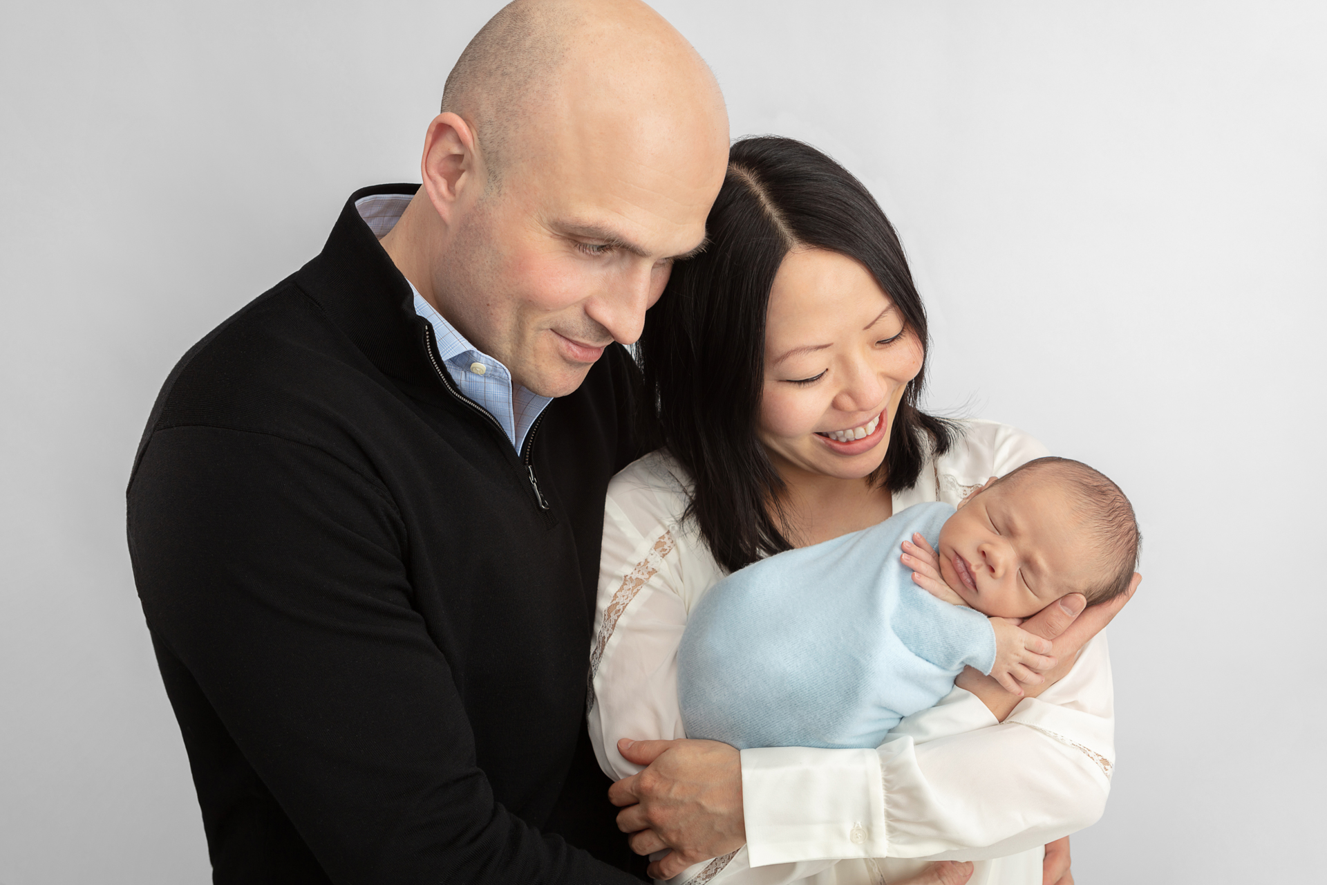 father, mother hold their newborn baby boy and look down lovingly at him; Karen Kahn