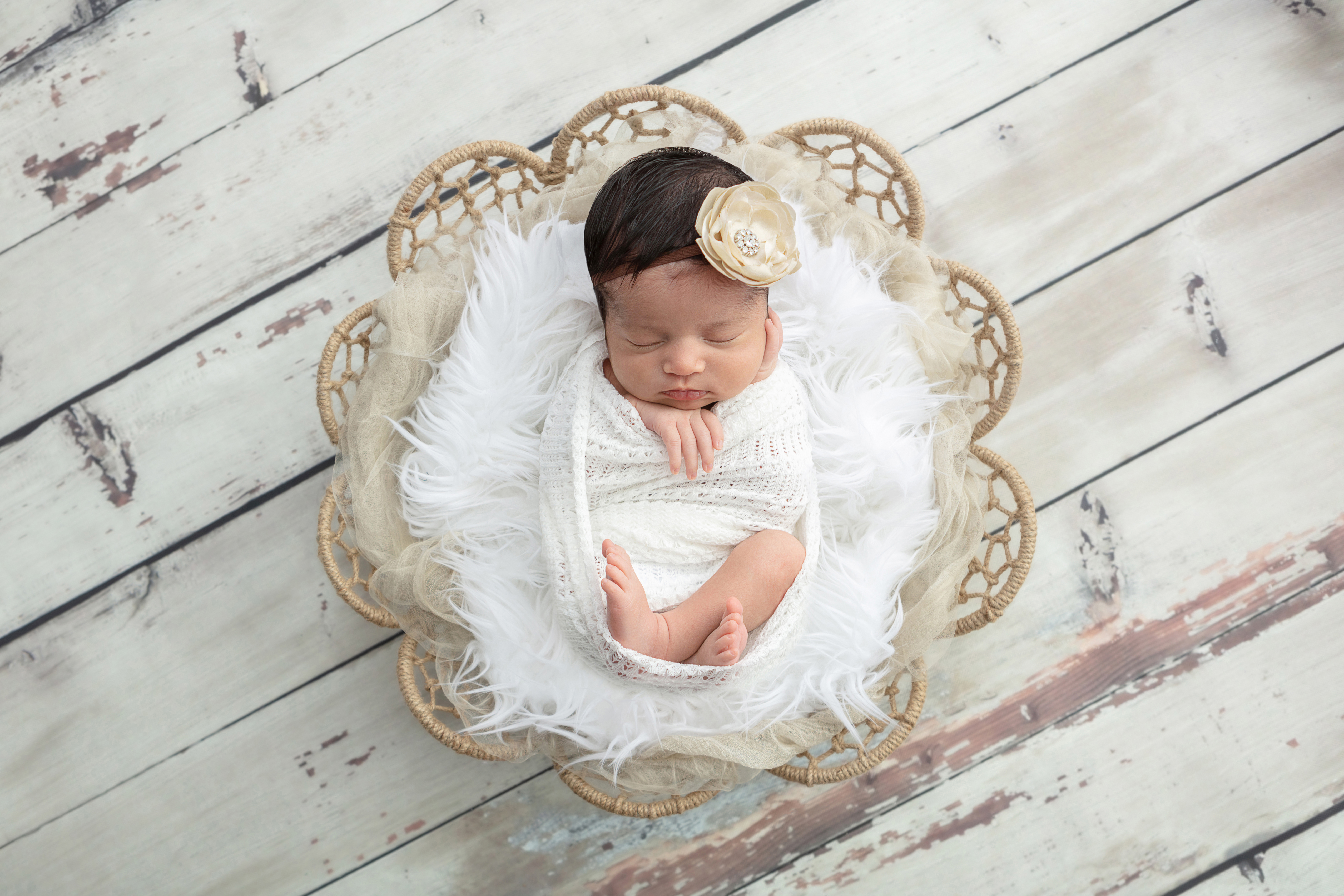 newborn baby girl wrapped in an open knit white swaddle, resting on two toned flokati
