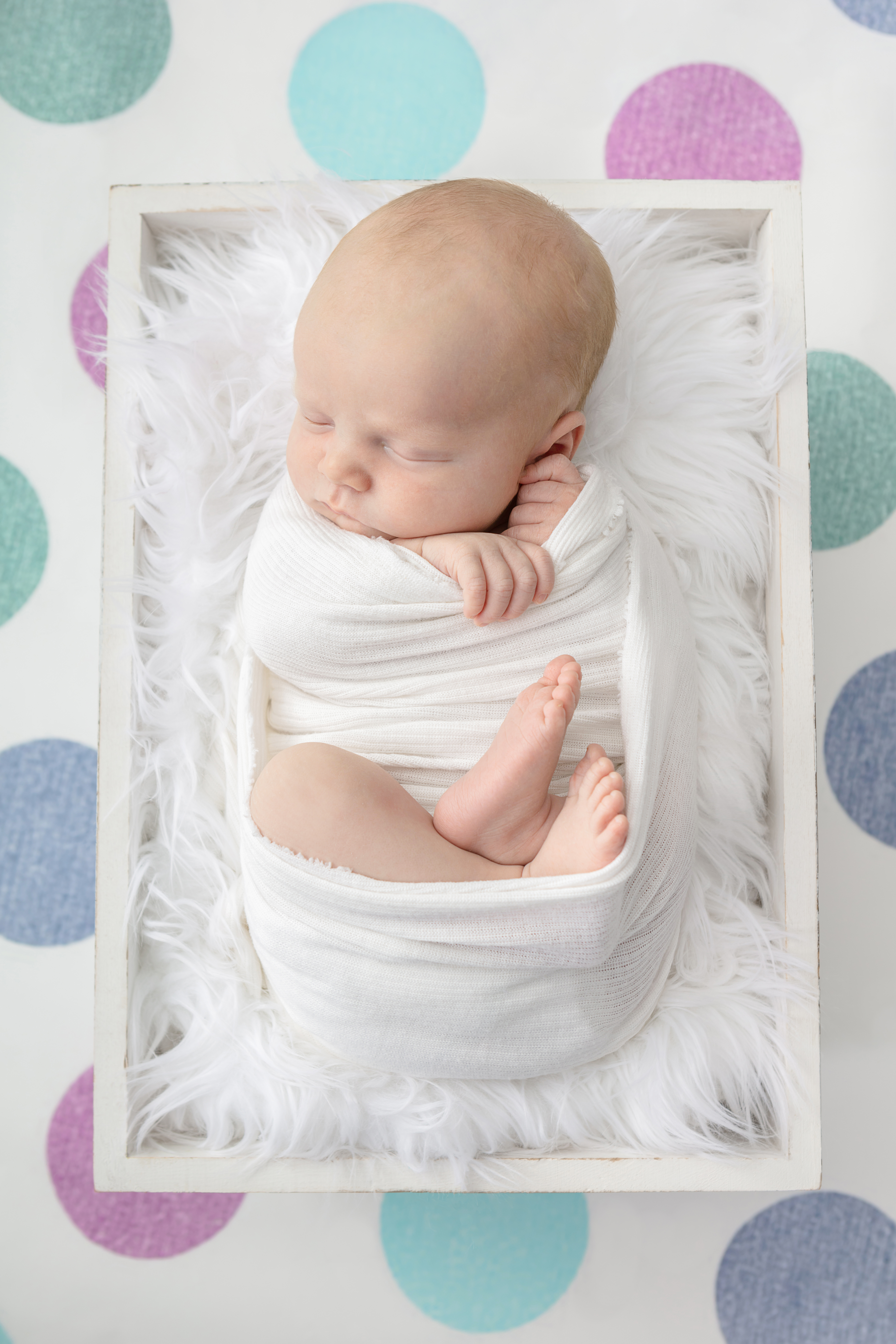 newborn baby boy swaddled in white with his hands and feet peeking out; white flokati