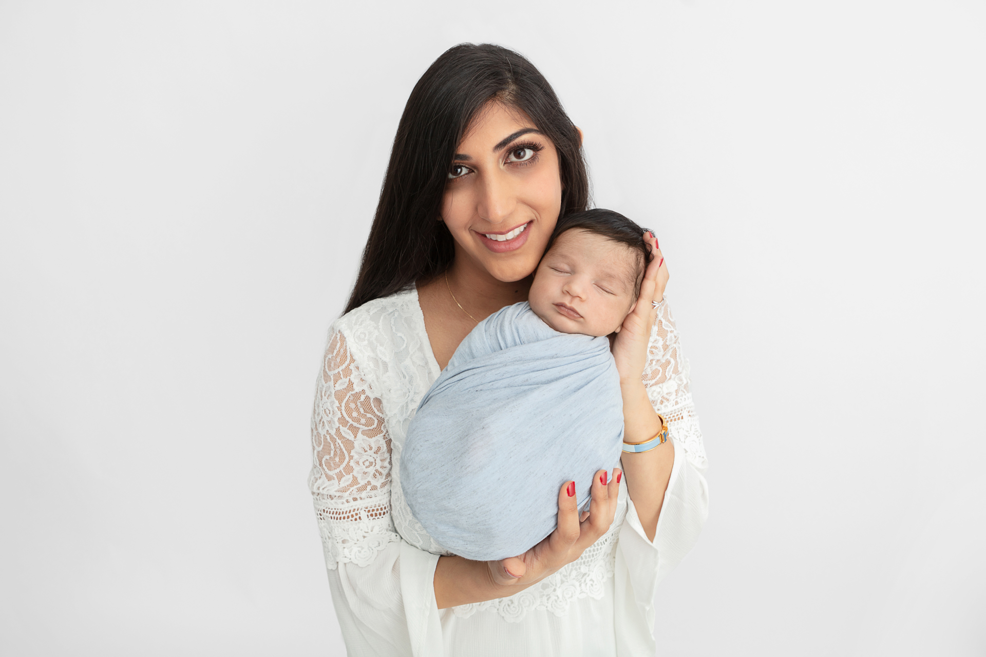 new mom with long dark hair and a white lace dress, holding her son who is swaddled in light blue