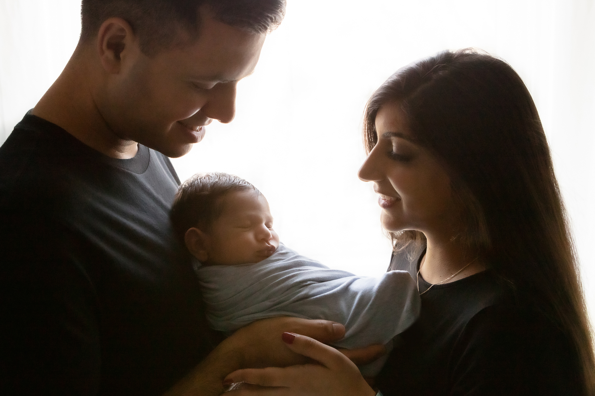 backlit, silhouetted image of a new family of three; father, mother, newborn baby boy