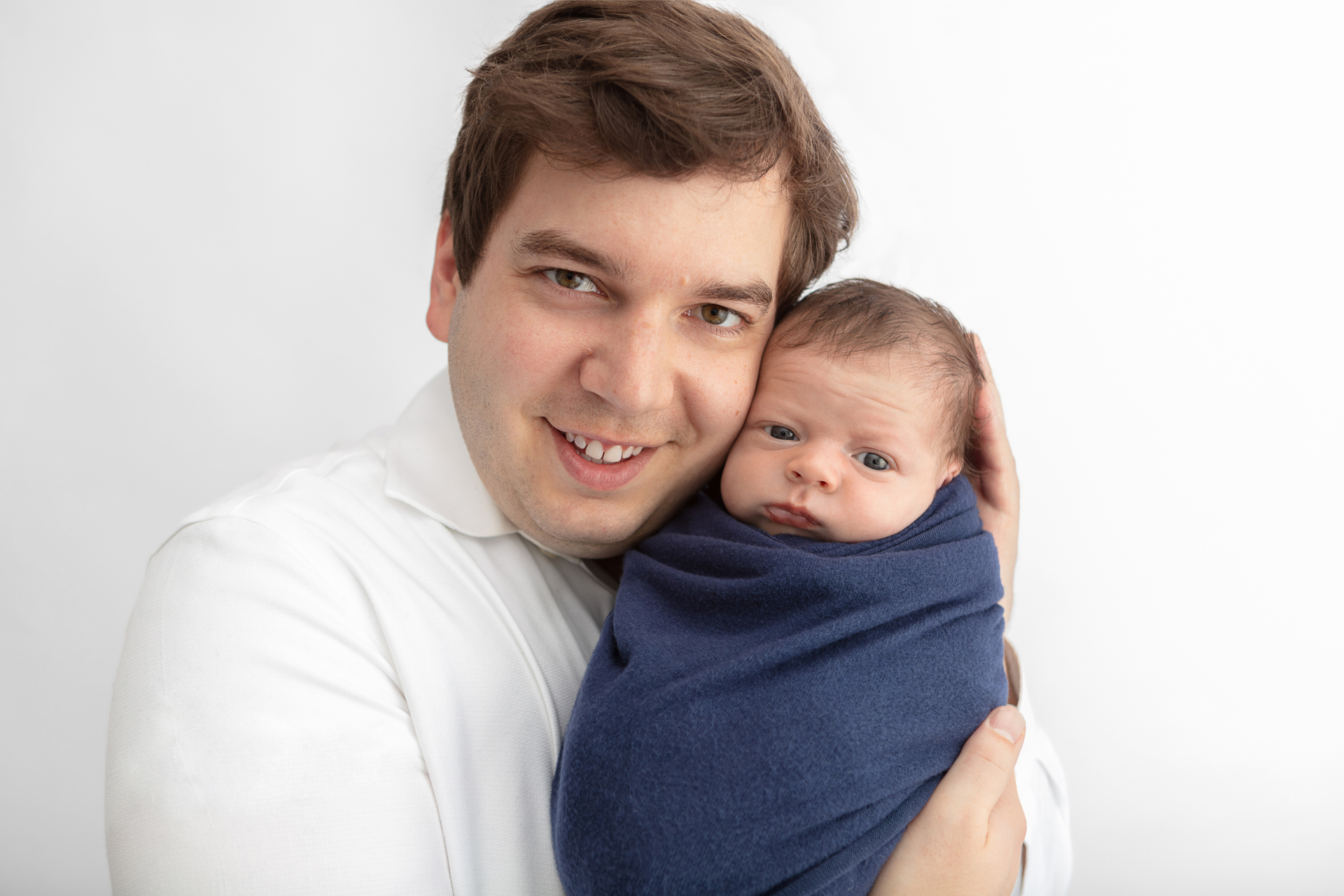 dad holding his newborn son close to his face; the baby is wrapped in a navy colored swaddle blanket