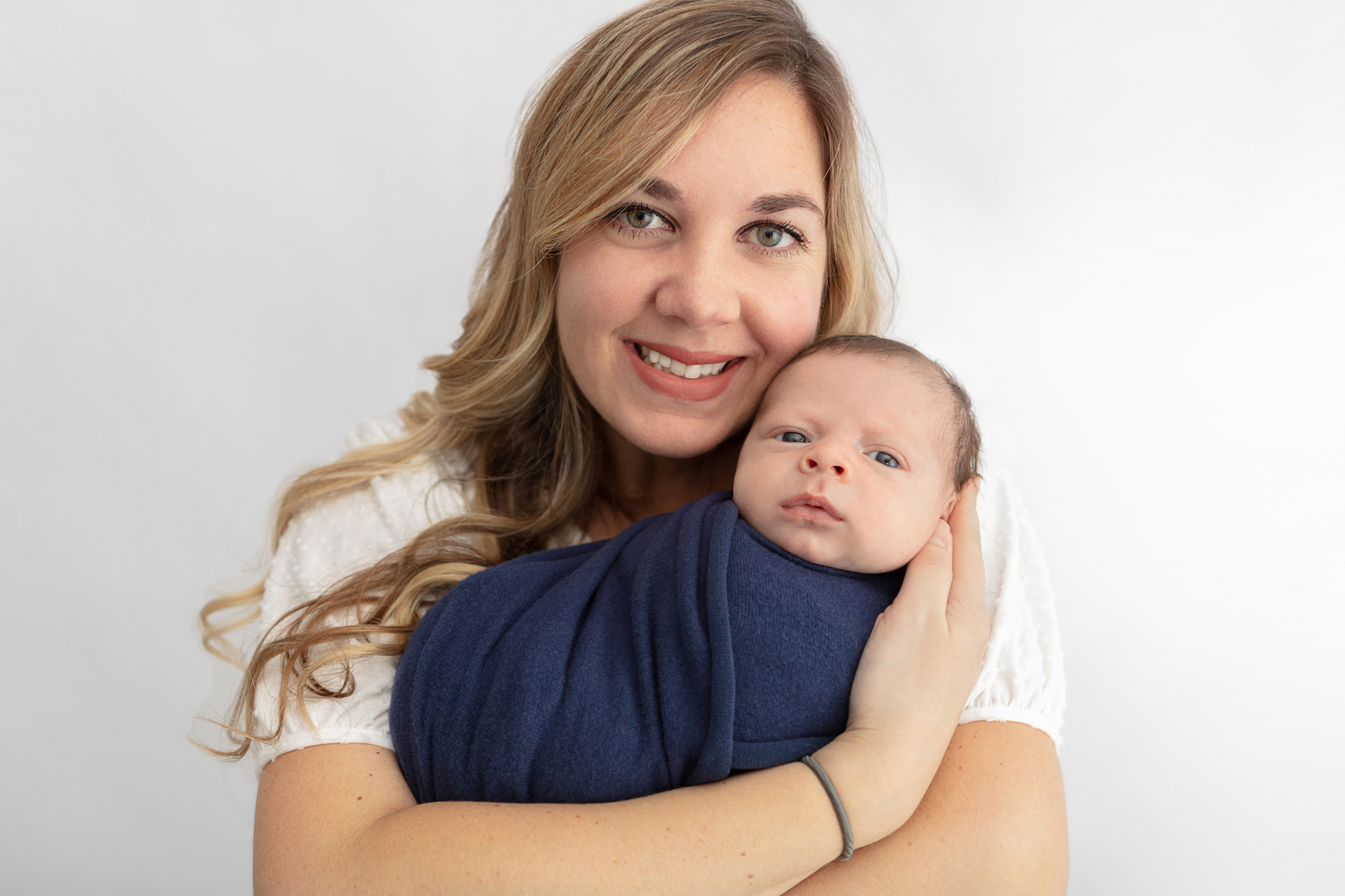 mom with long golden blonde hair smiling at the camera and cradling her newborn baby in her arms