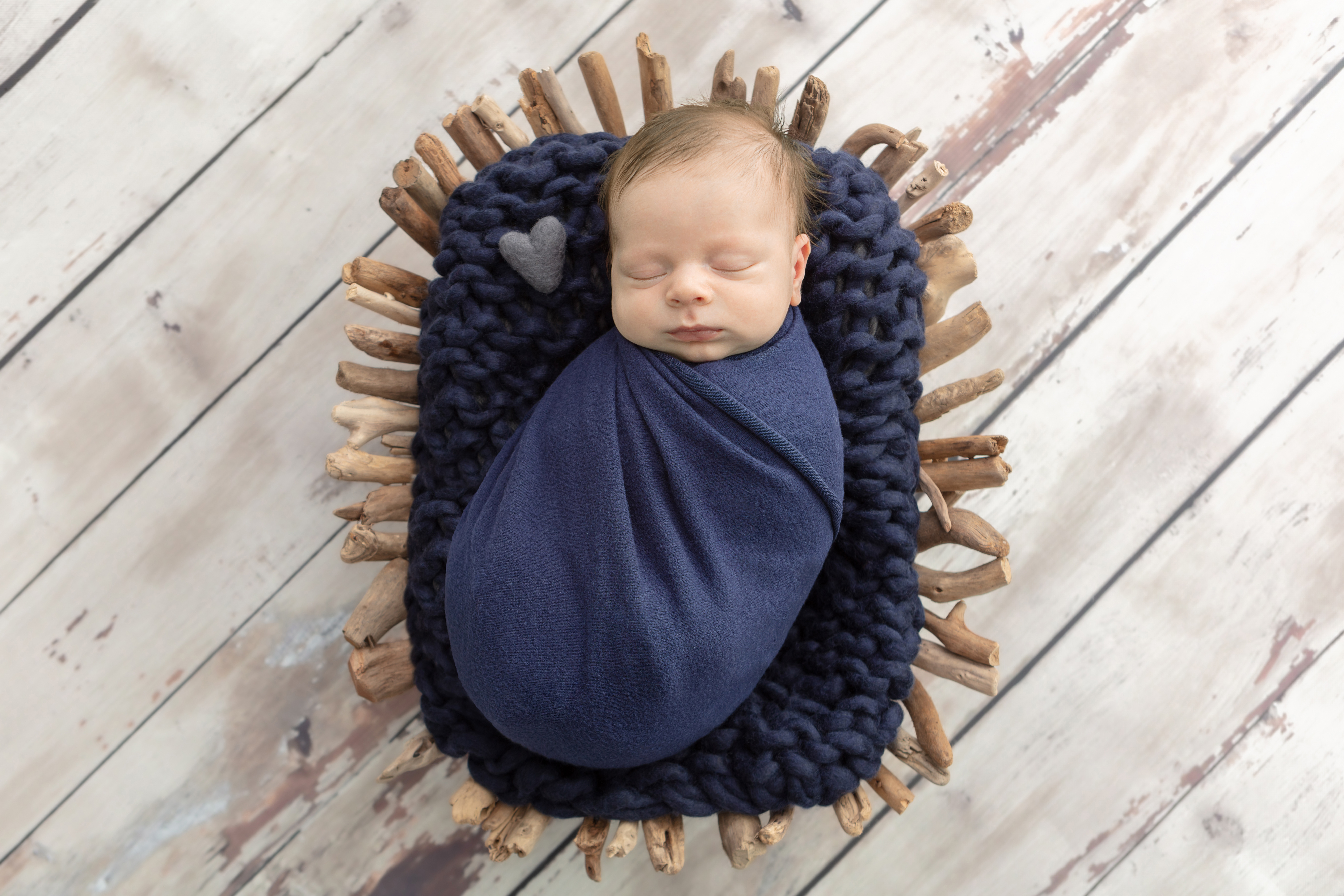 newborn baby boy wrapped in navy and asleep on top of a chunky knit blanket in a driftwood basket