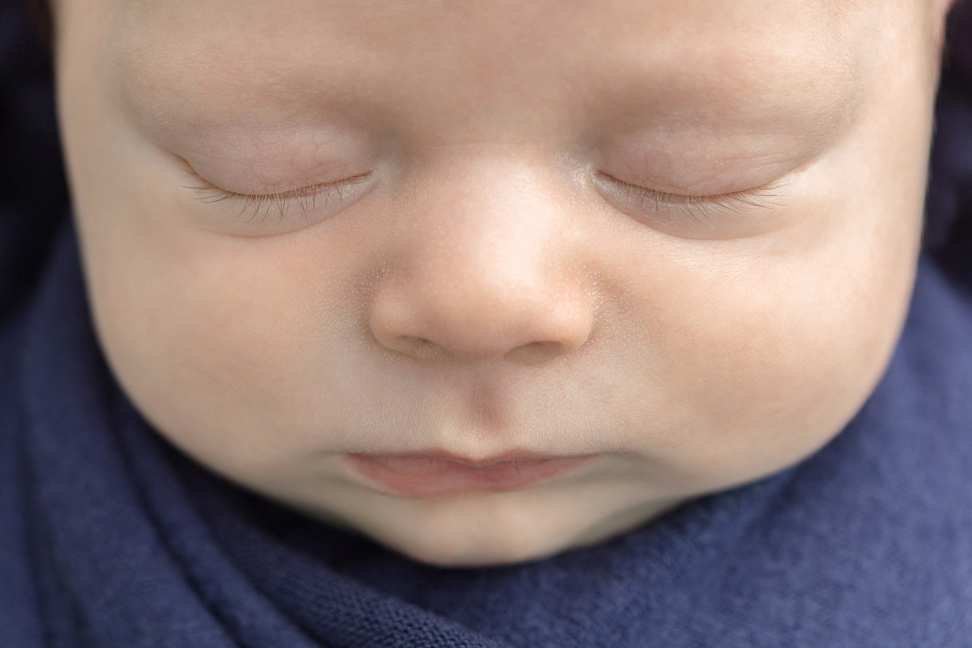 close up features of a newborn baby's face, eyes, nose, lips; baby wrapped in a navy swaddle