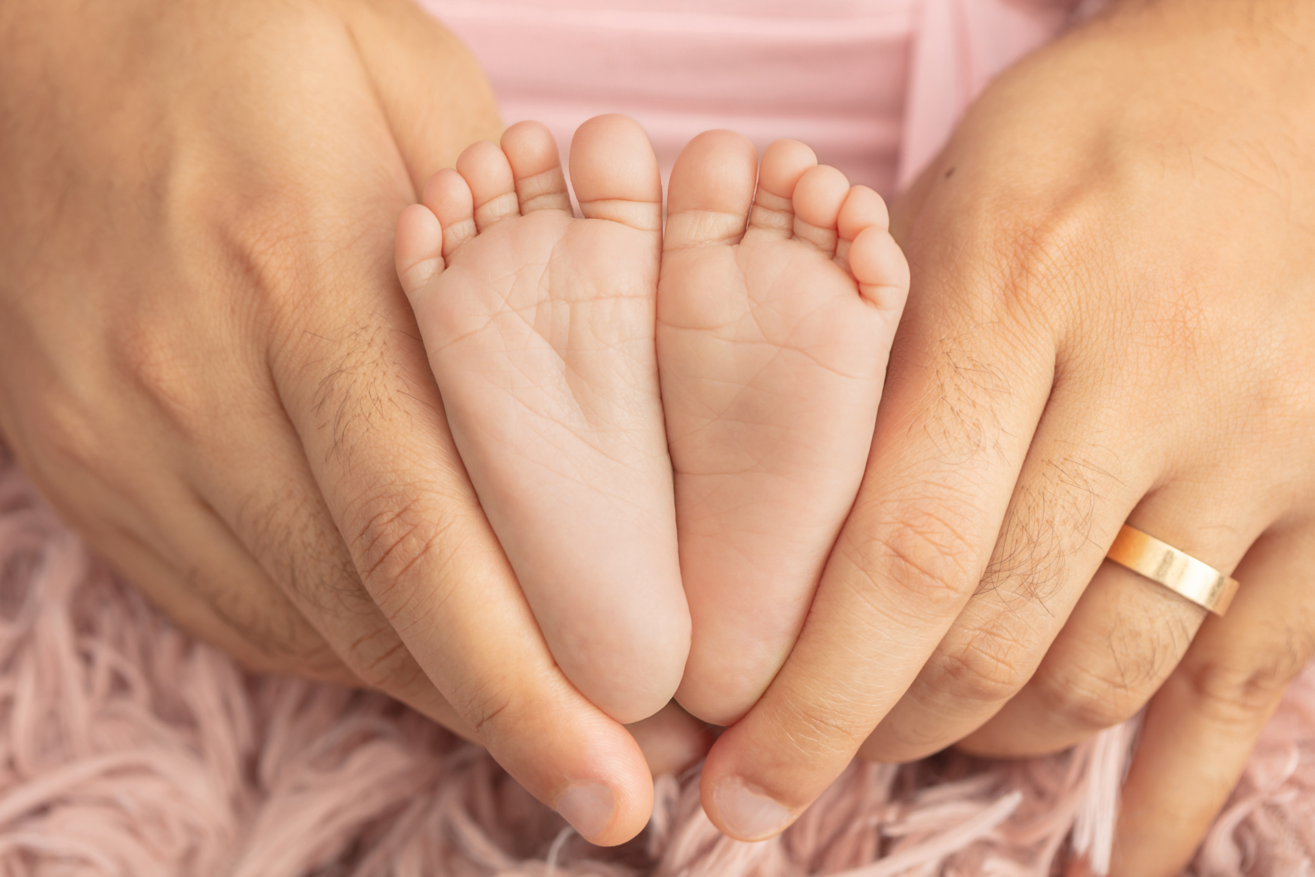 father's hands holding newborn baby girl's feet; dusty rose flokati; light pink swaddle