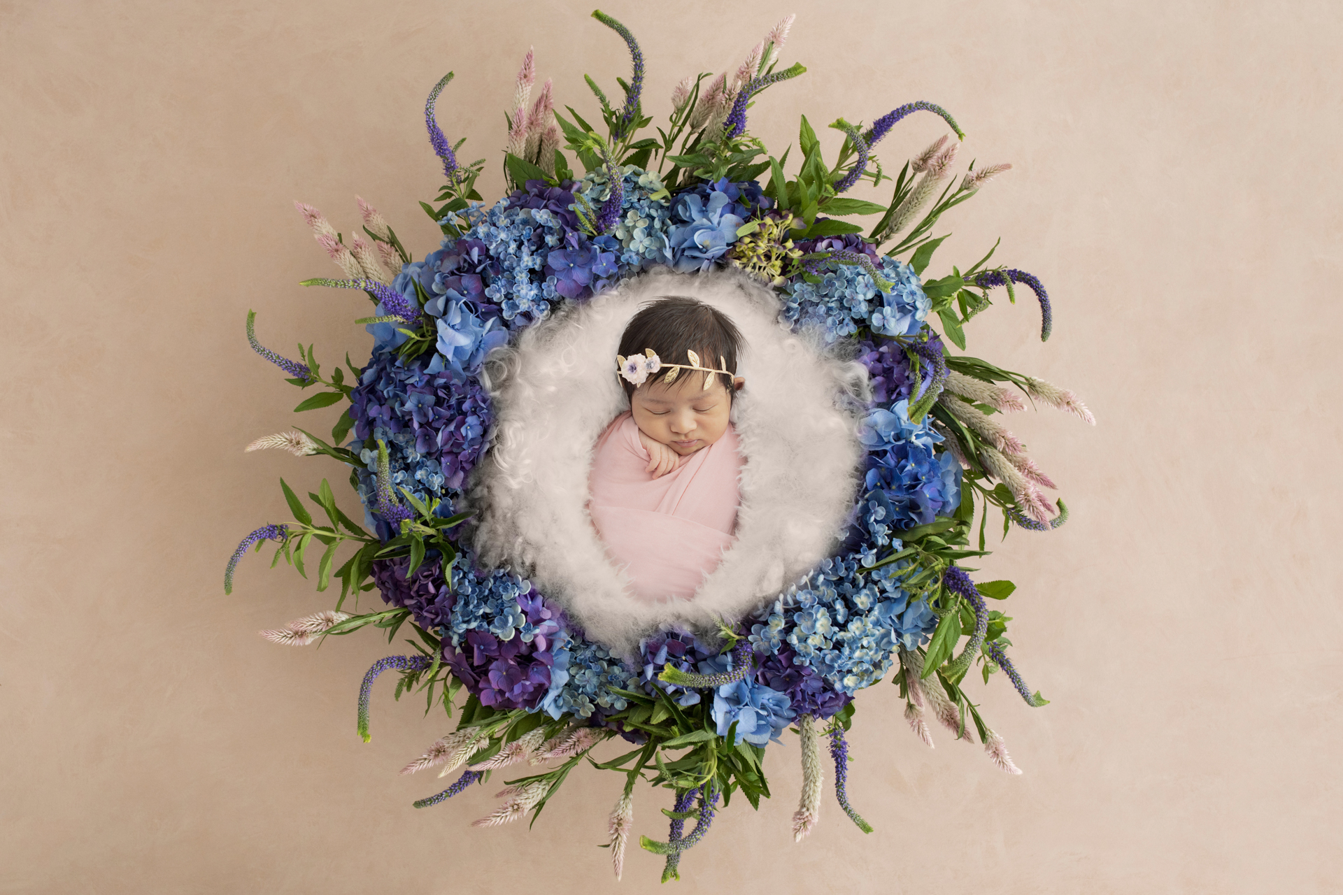 newborn baby girl wrapped in light pink and wearing a delicate headband; white fluff in a basket; floral newborn image