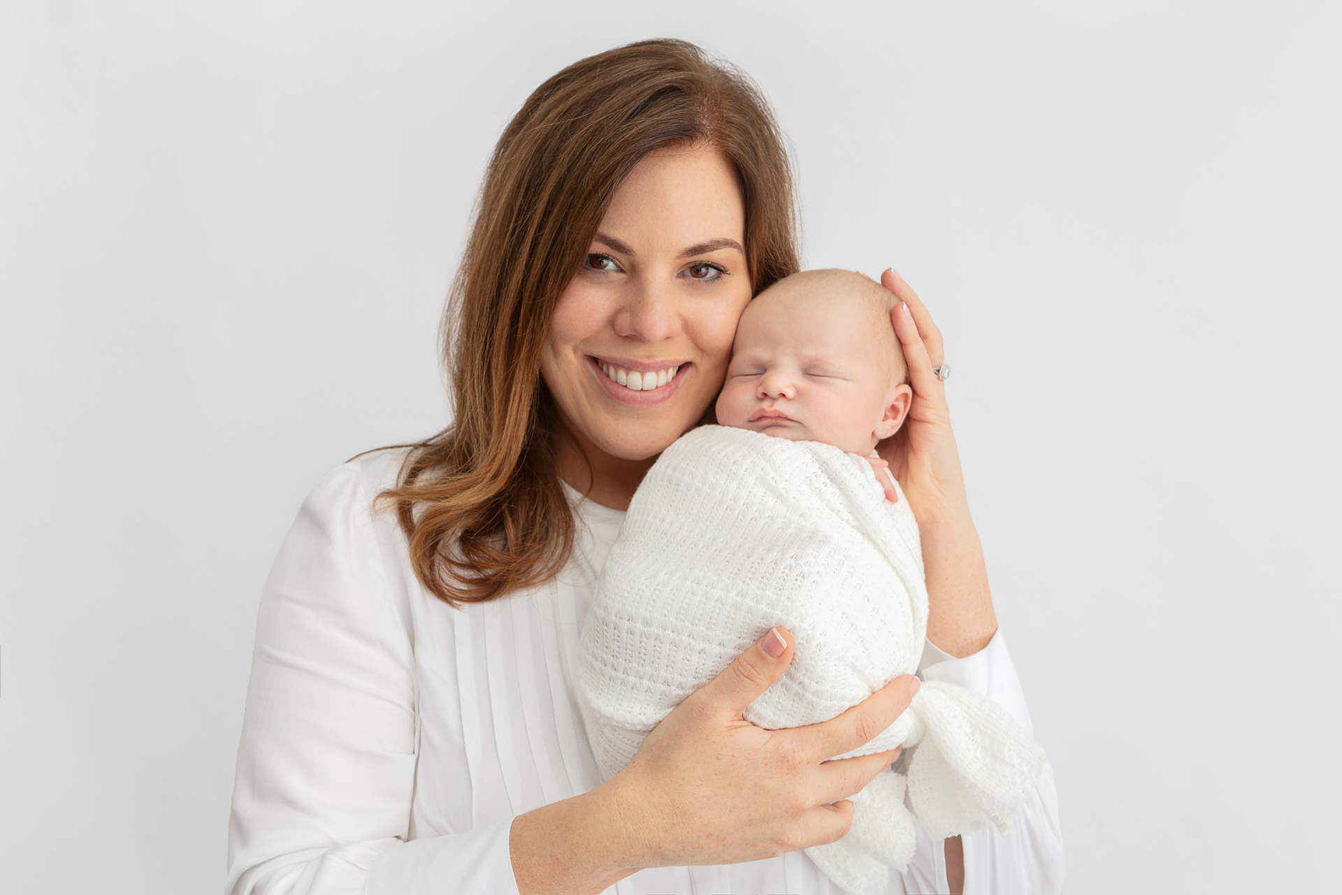 smiling Irish mom holding her newborn son against her cheek; mother and baby are in white