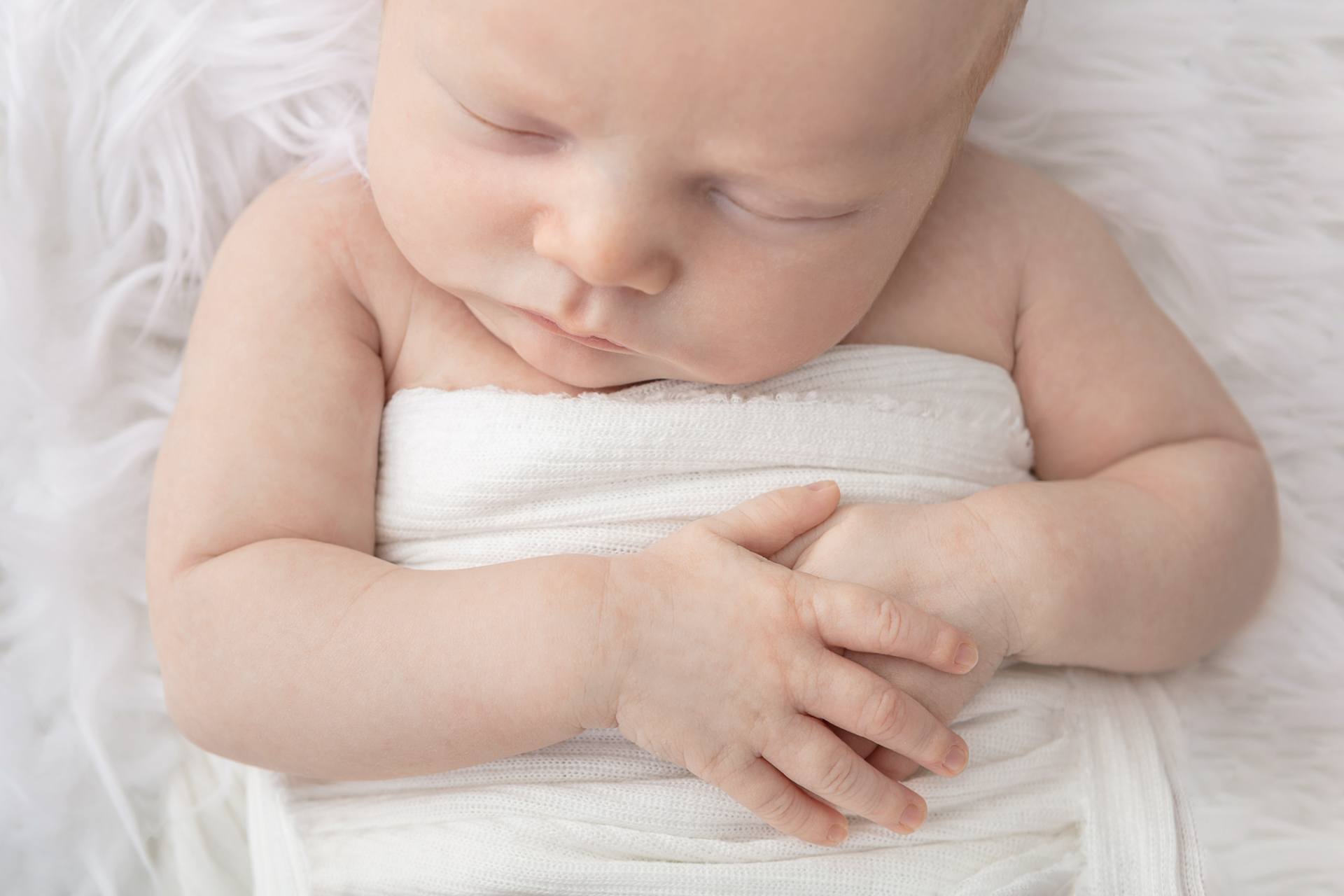 newborn baby boy details with his hands folded across himself; white muslin swaddle