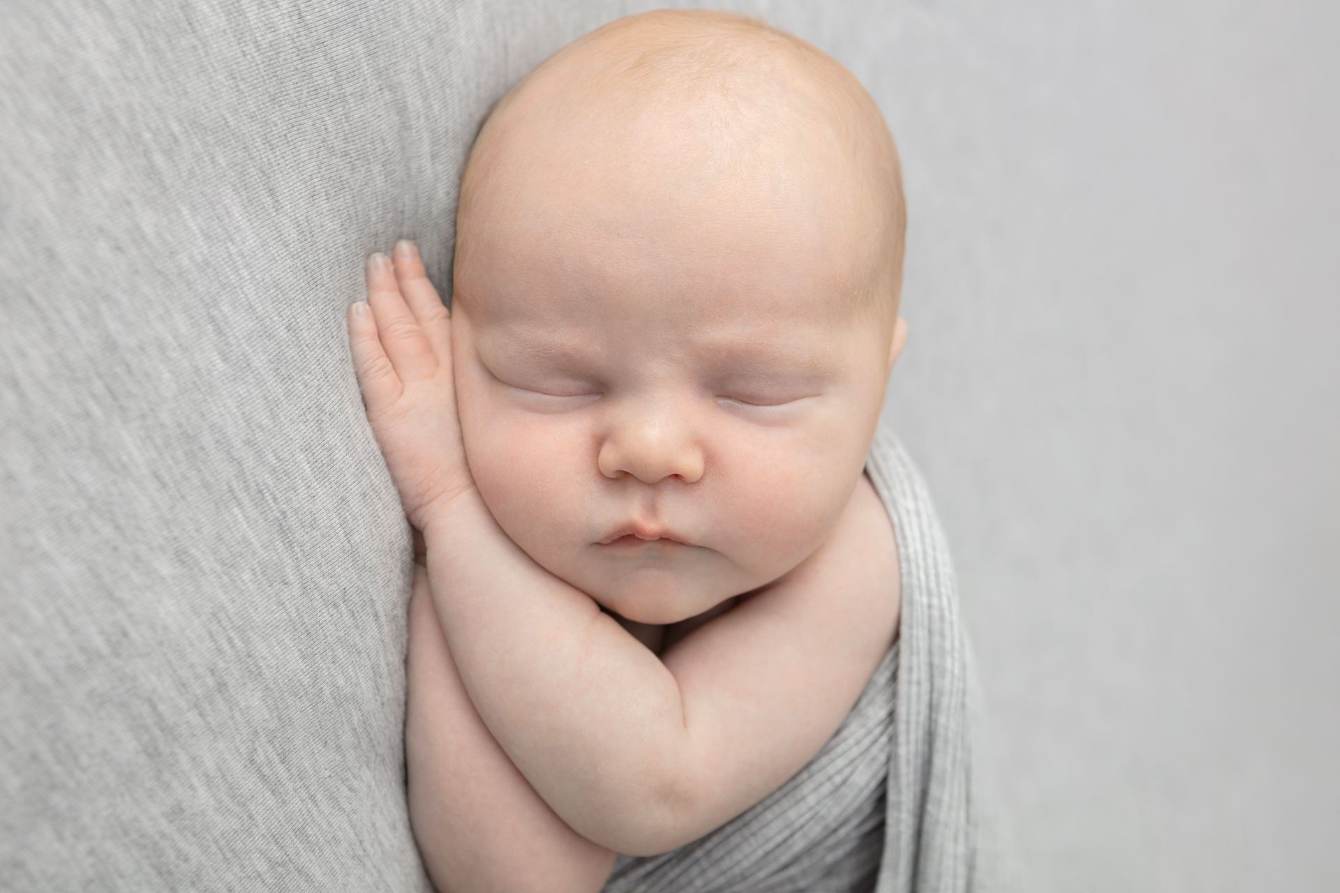 redhead newborn baby boy asleep on his hands; gray jersey backdrop; knit gray swaddle
