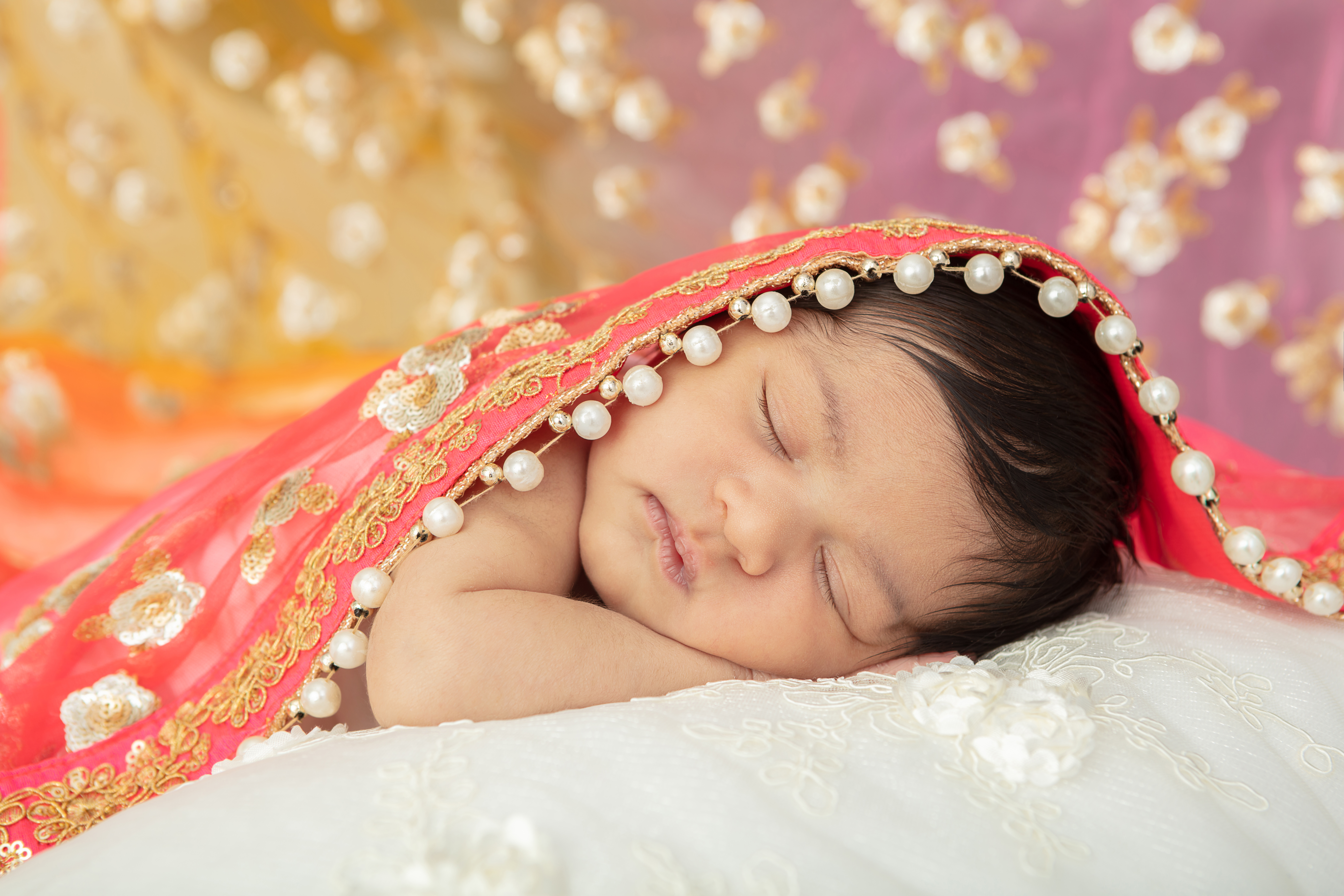 newborn Indian baby girl resting on a textured cream colored blanket, draped in her mother's sari