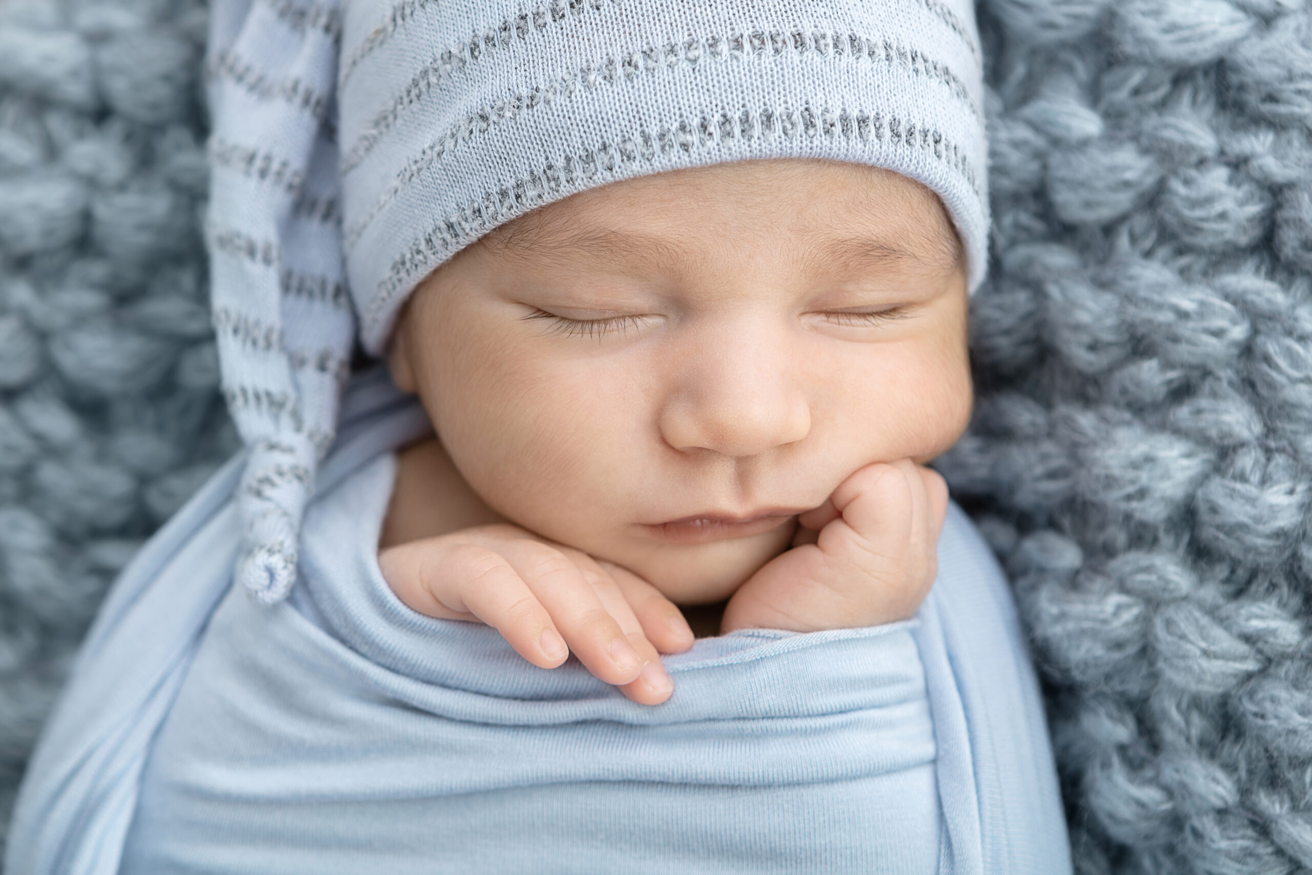 Newborn portrait session in the studio with baby boy wrapped in light blue laying on a soft knit light blue fabric and an adorable sleepy night cap hat in blue