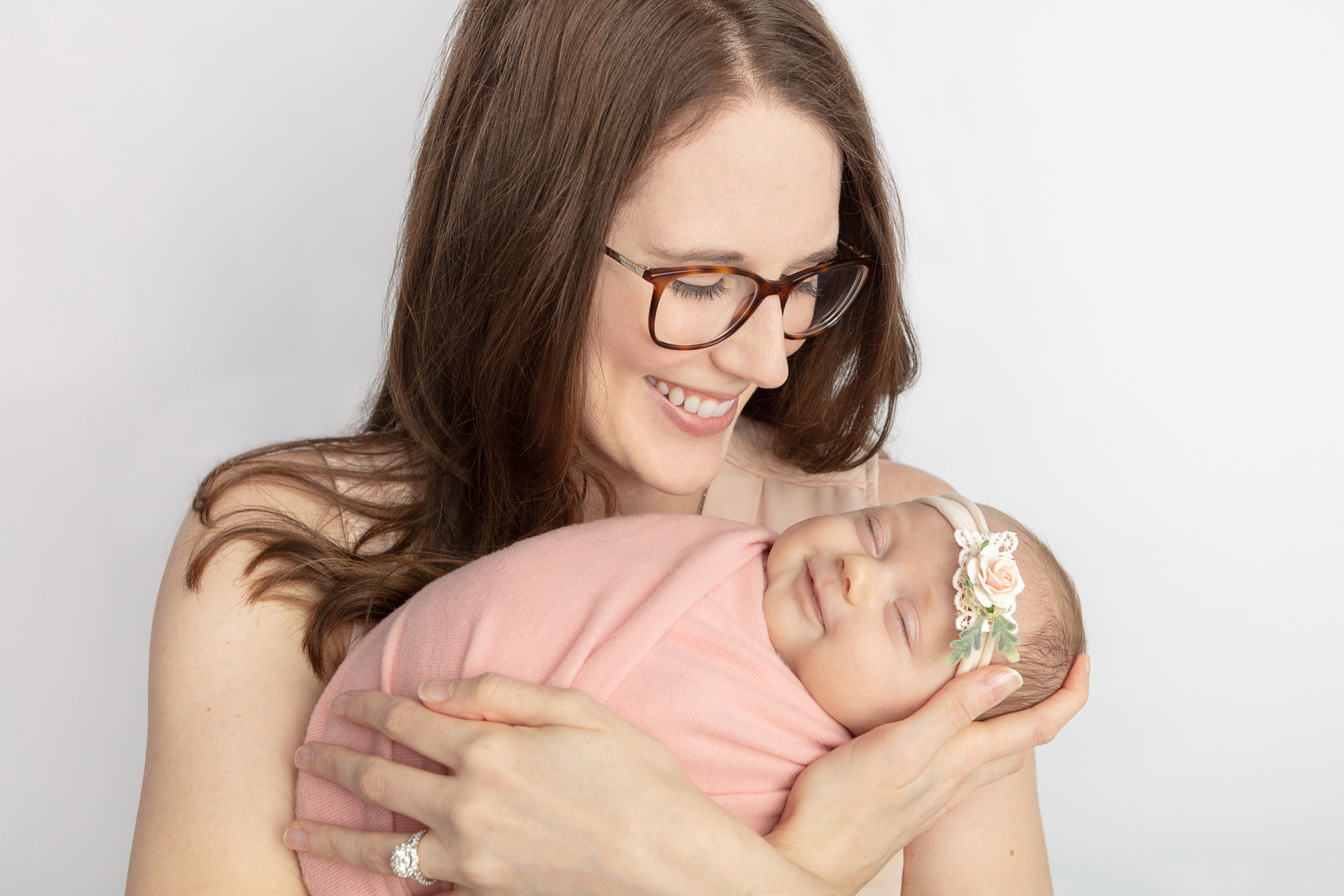 smiling new mom with auburn hair and glasses, looking down at her smiling newborn daughter