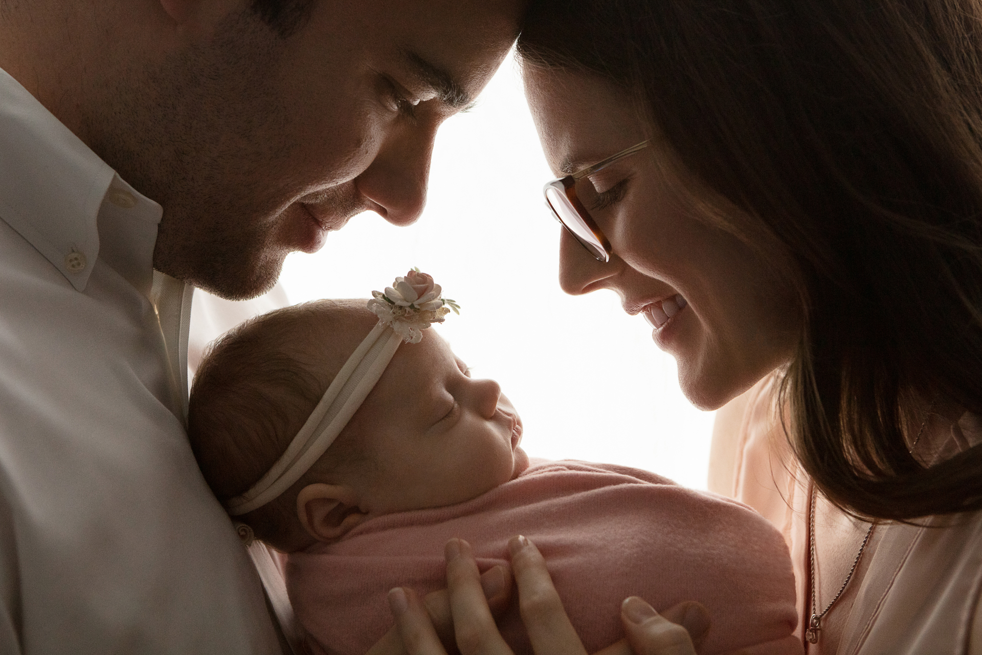 backlit silhouetted image of a new dad and new mother smiling down at their daughter