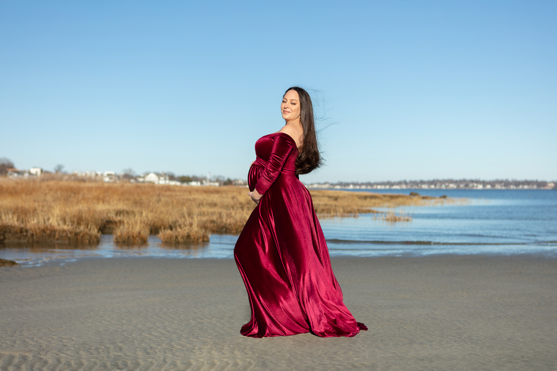 pregnant mama to be wearing a red velvet dress, standing on the beach at Tod's Point; Looking Up Photography