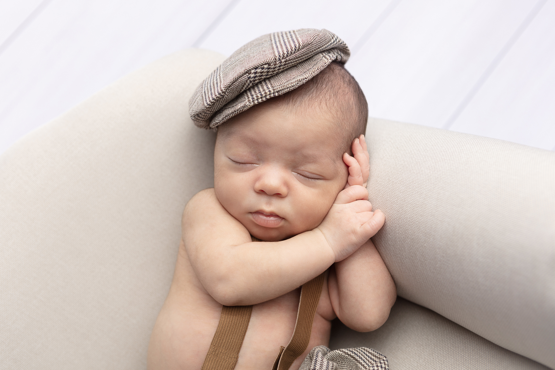 newborn baby boy with his hands folded under his head, wearing a plaid cap; CT baby photography