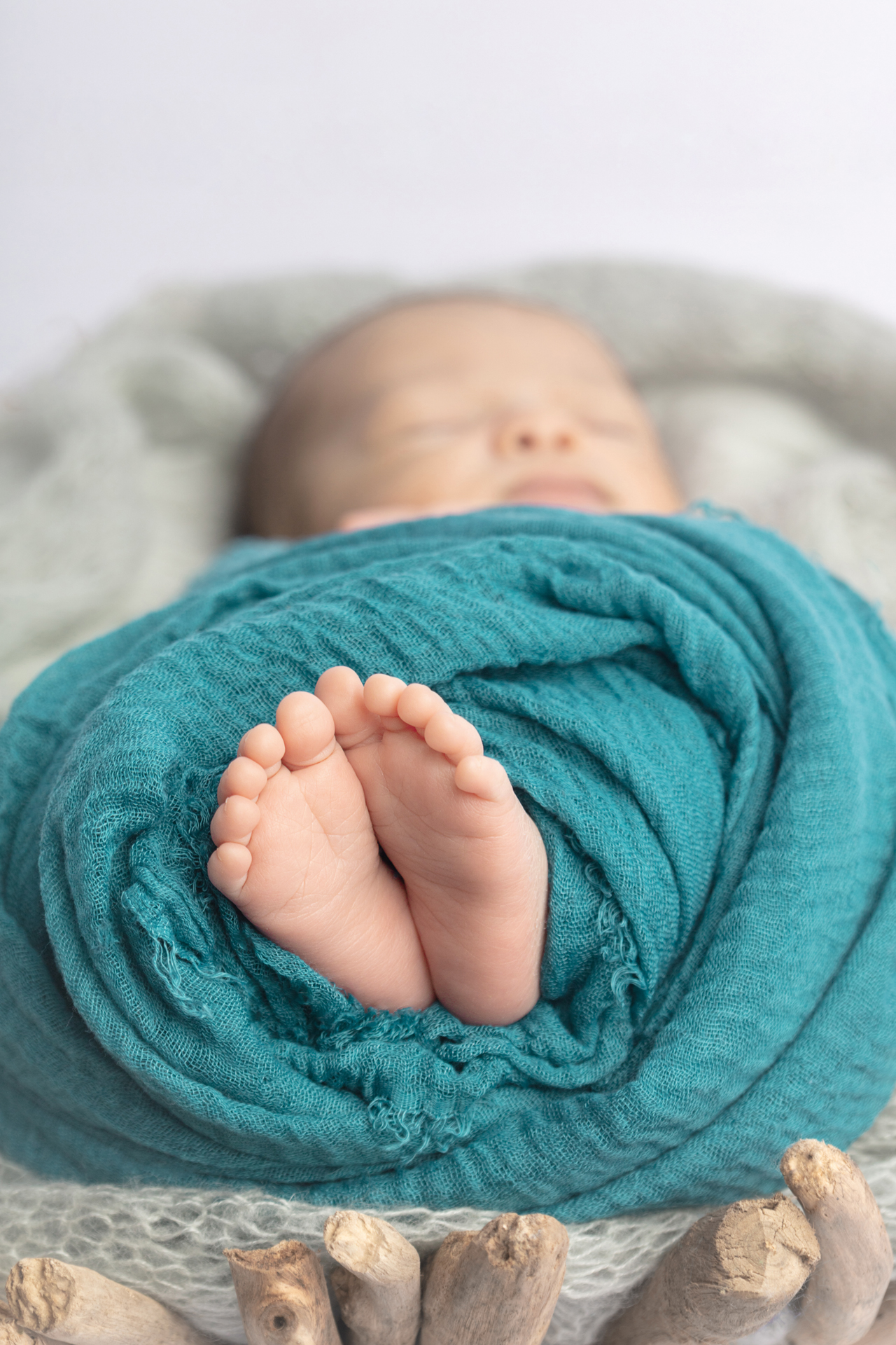 newborn baby feet and toes peeking from a dusty turquoise swaddle; driftwood peeking from the bottom of the photo