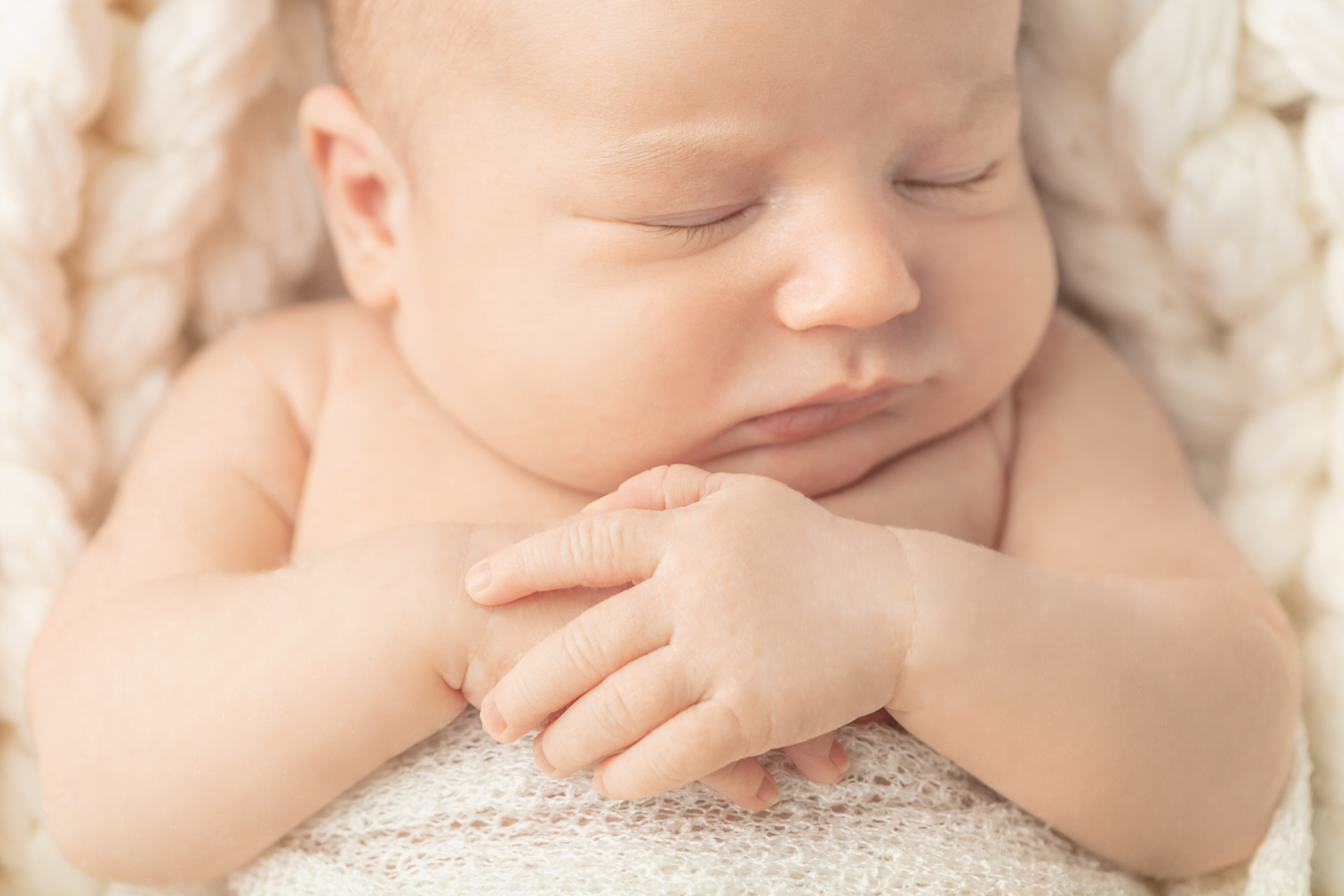 newborn baby boy with his hands folded across his chest; ivory chunky knit blanket backdrop; Looking Up Photography