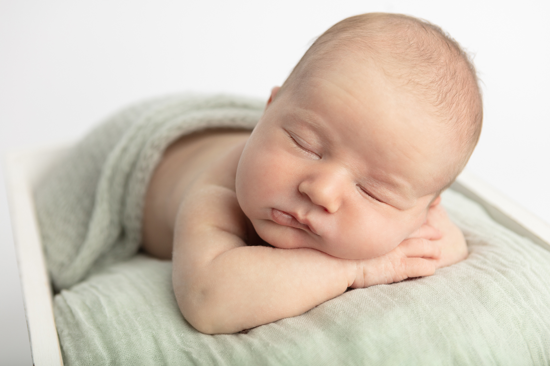 newborn baby boy sleeping with his hands folded underneath him; Looking Up Photography
