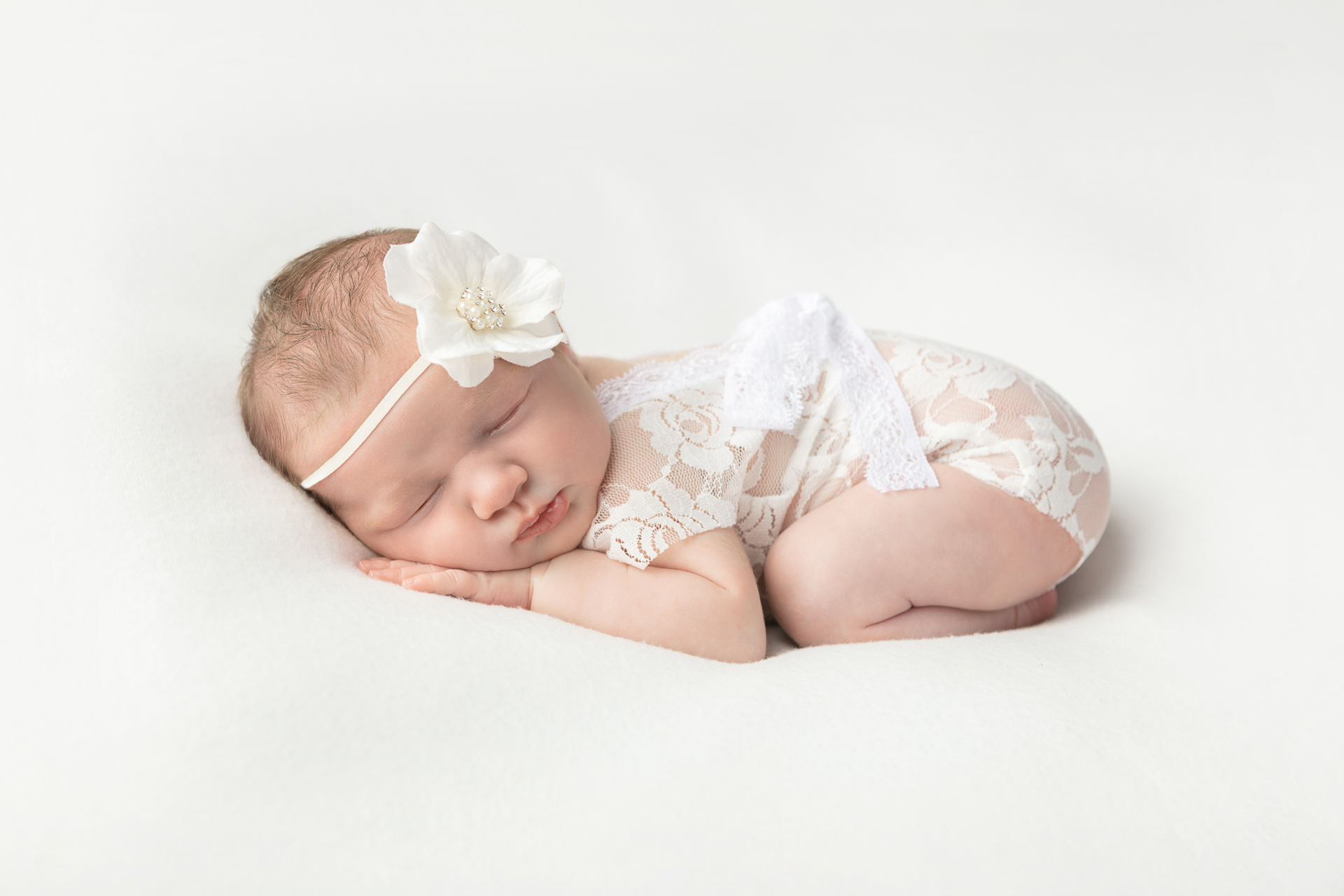newborn baby girl in lace onesie and wearing a large white flower headband
