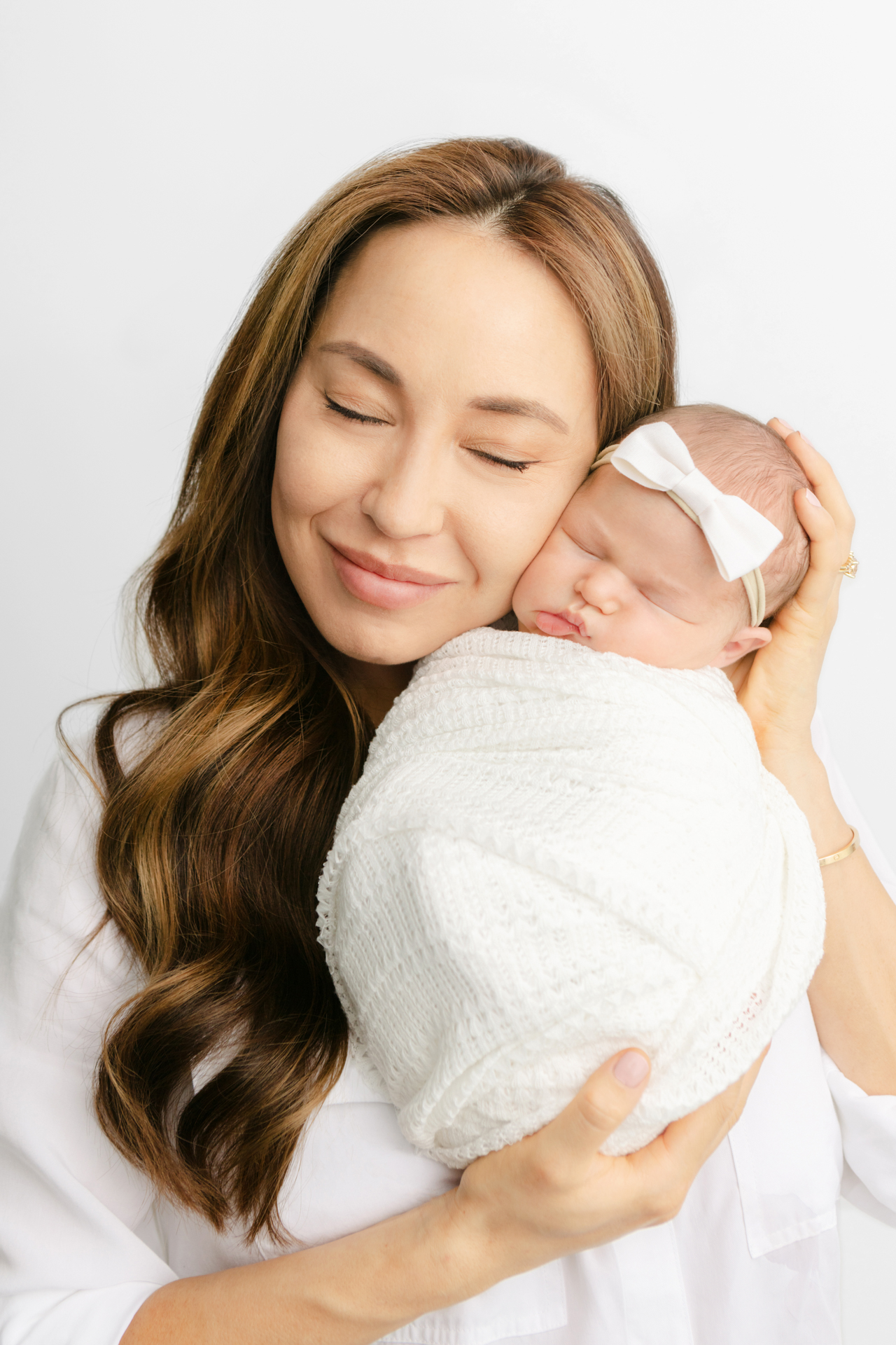 mom with long, wavy, honey brunette hair, closing her eyes and holding her newborn